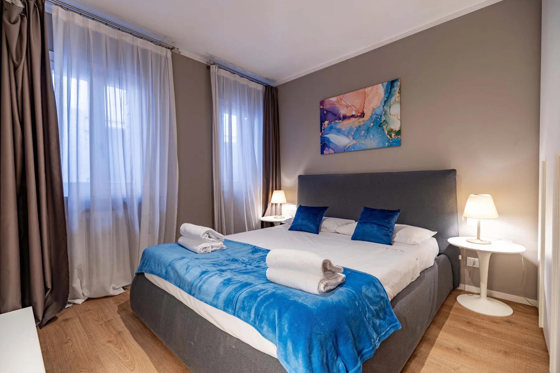 A bedroom with a bed dressed in white linens and a blue blanket.