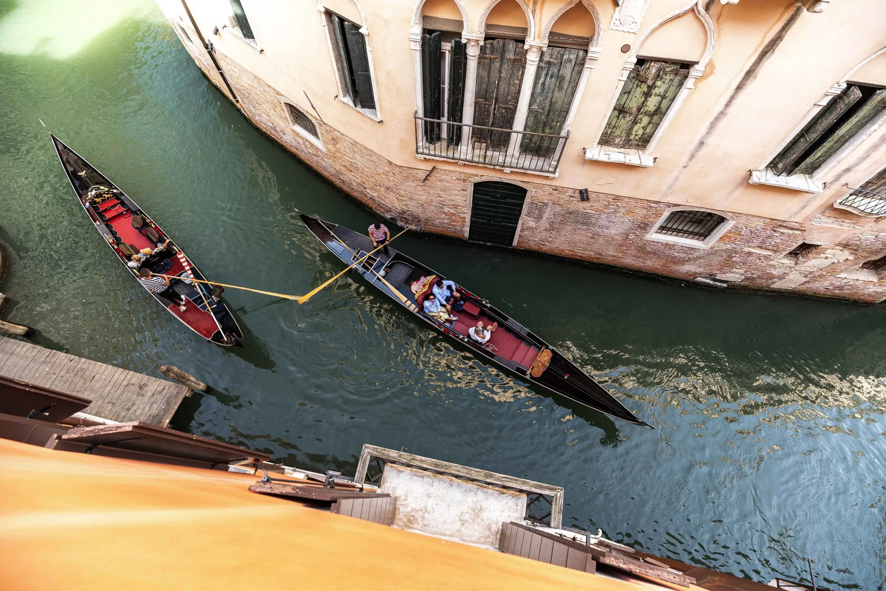 A canal runs beside a pale building, with two gondolas on the water.