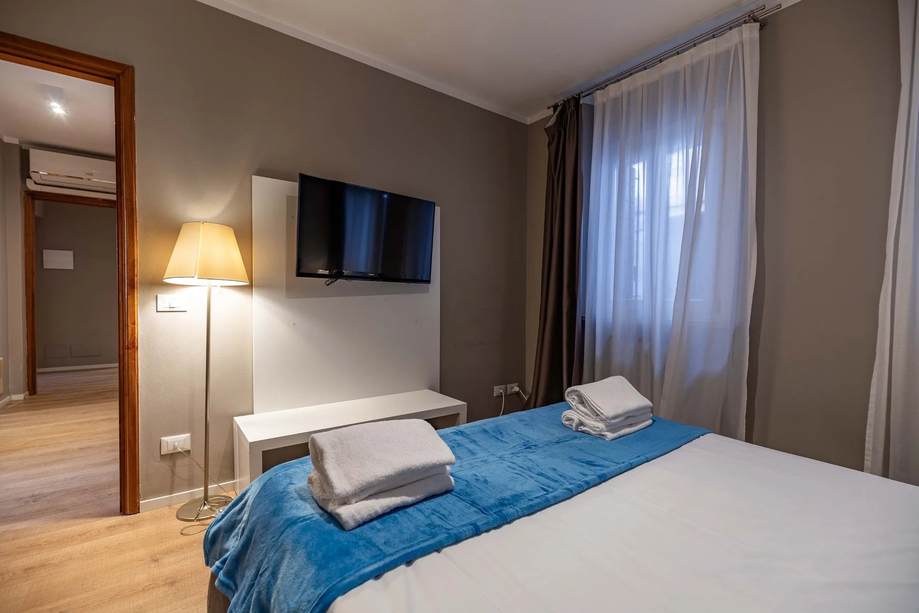 A bedroom with a neatly made bed and a wall-mounted television.