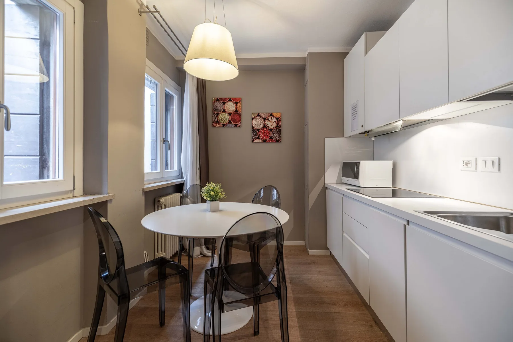 Una cocina compacta con una mesa redonda y sillas transparentes junto a las ventanas.