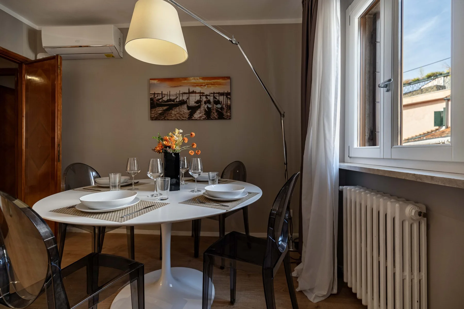 A dining area with a round table set with plates and glasses beside a window.