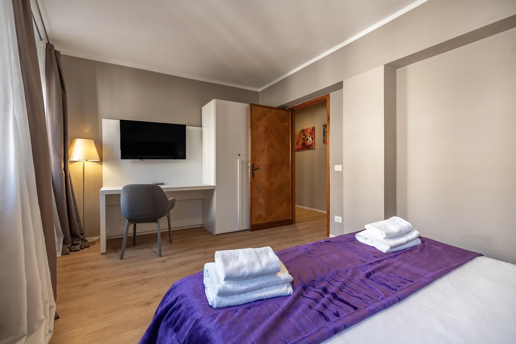 A bedroom with a purple bedspread, a desk, and a wall-mounted television.
