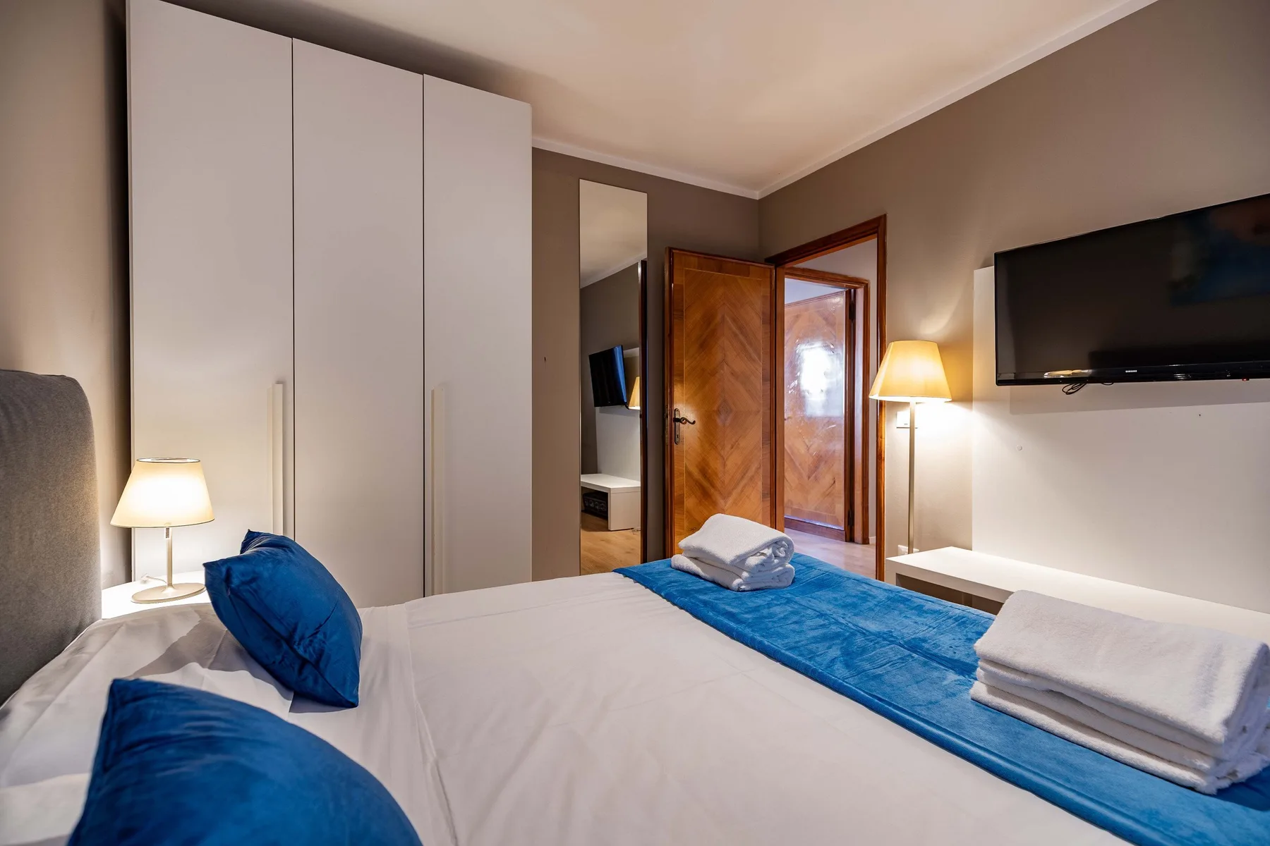 A bedroom with a neatly made bed, blue bedding, and a wall-mounted television.