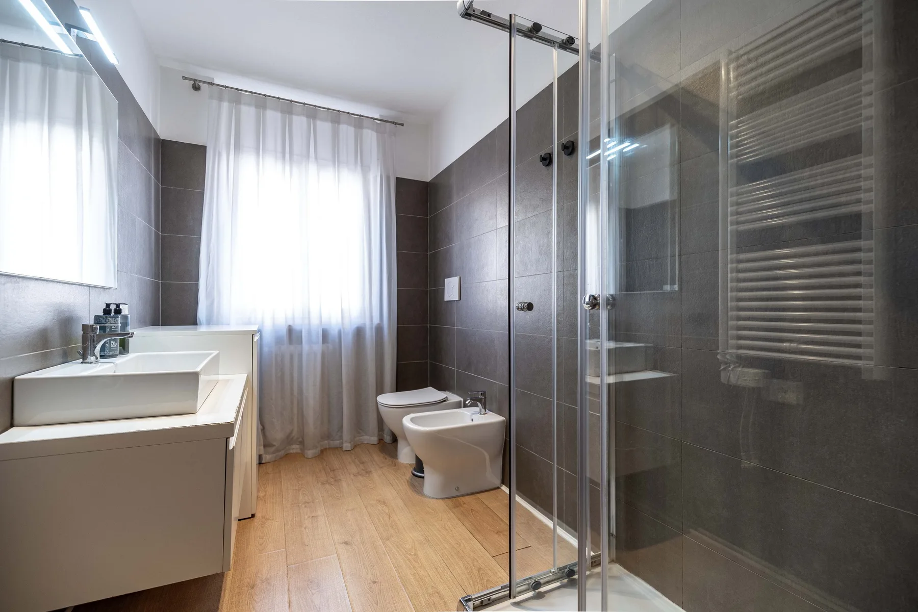 A bright bathroom with a sink, toilet, bidet, and glass shower.