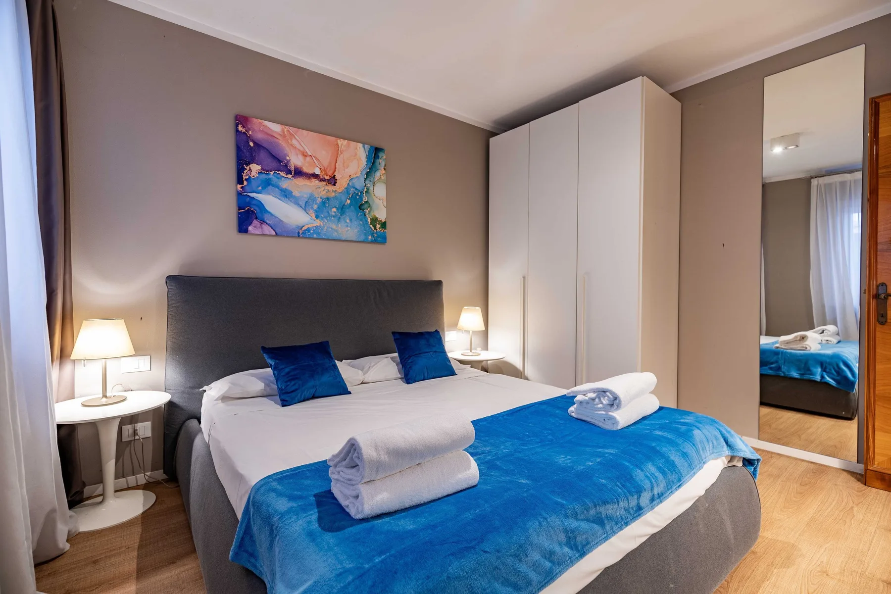 A bedroom with a bed dressed in blue and a wardrobe beside it.