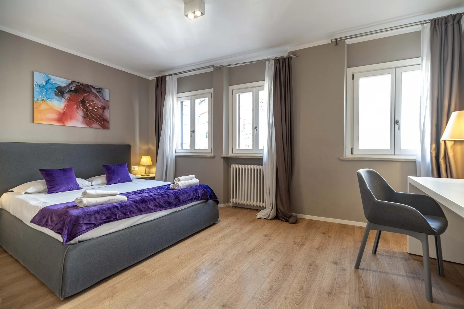 A bedroom with a bed, bedside tables, and windows along the wall.