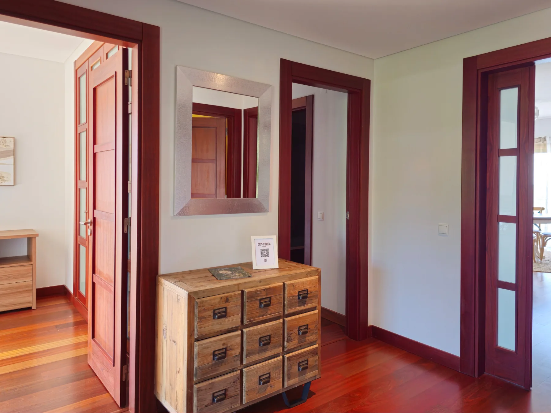 Pasillo interior con suelo de madera, puertas y una cómoda.