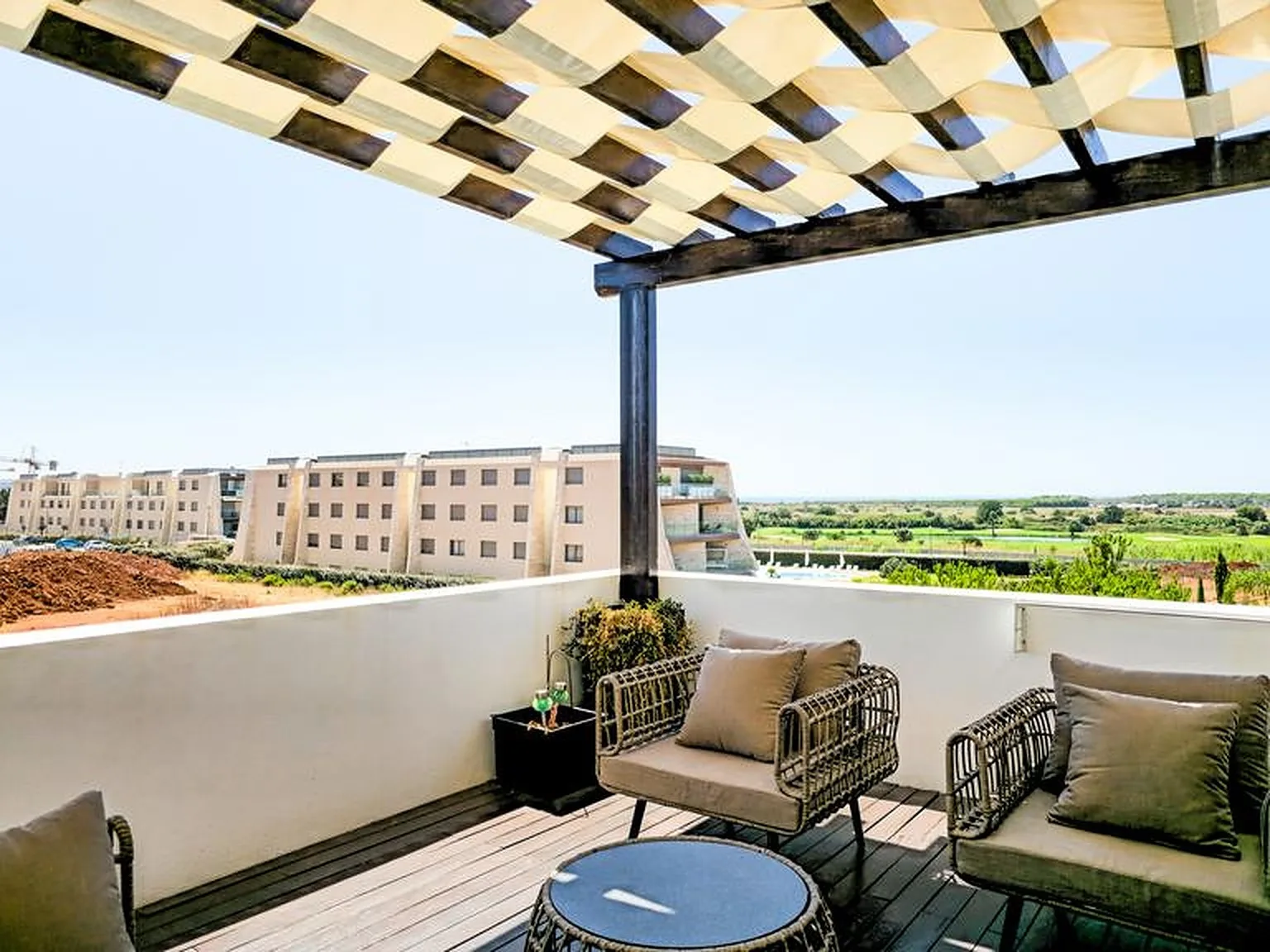 A furnished balcony with outdoor seating beneath a patterned shade canopy.