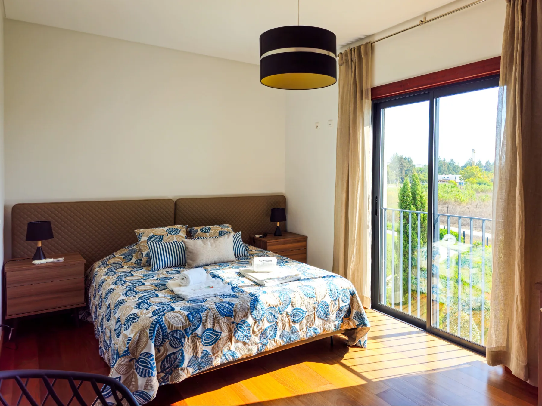A bedroom with a patterned bedspread and a glass door opening onto a balcony.