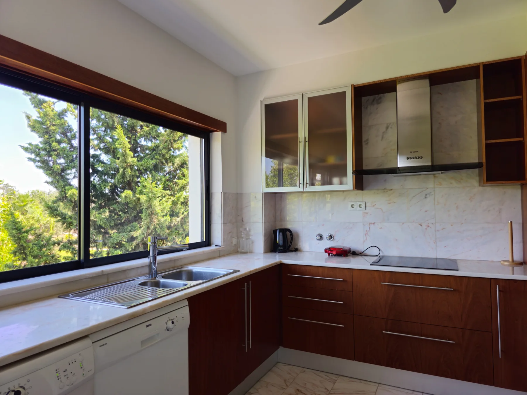 A bright kitchen with dark wood cabinets and a large window overlooking trees.