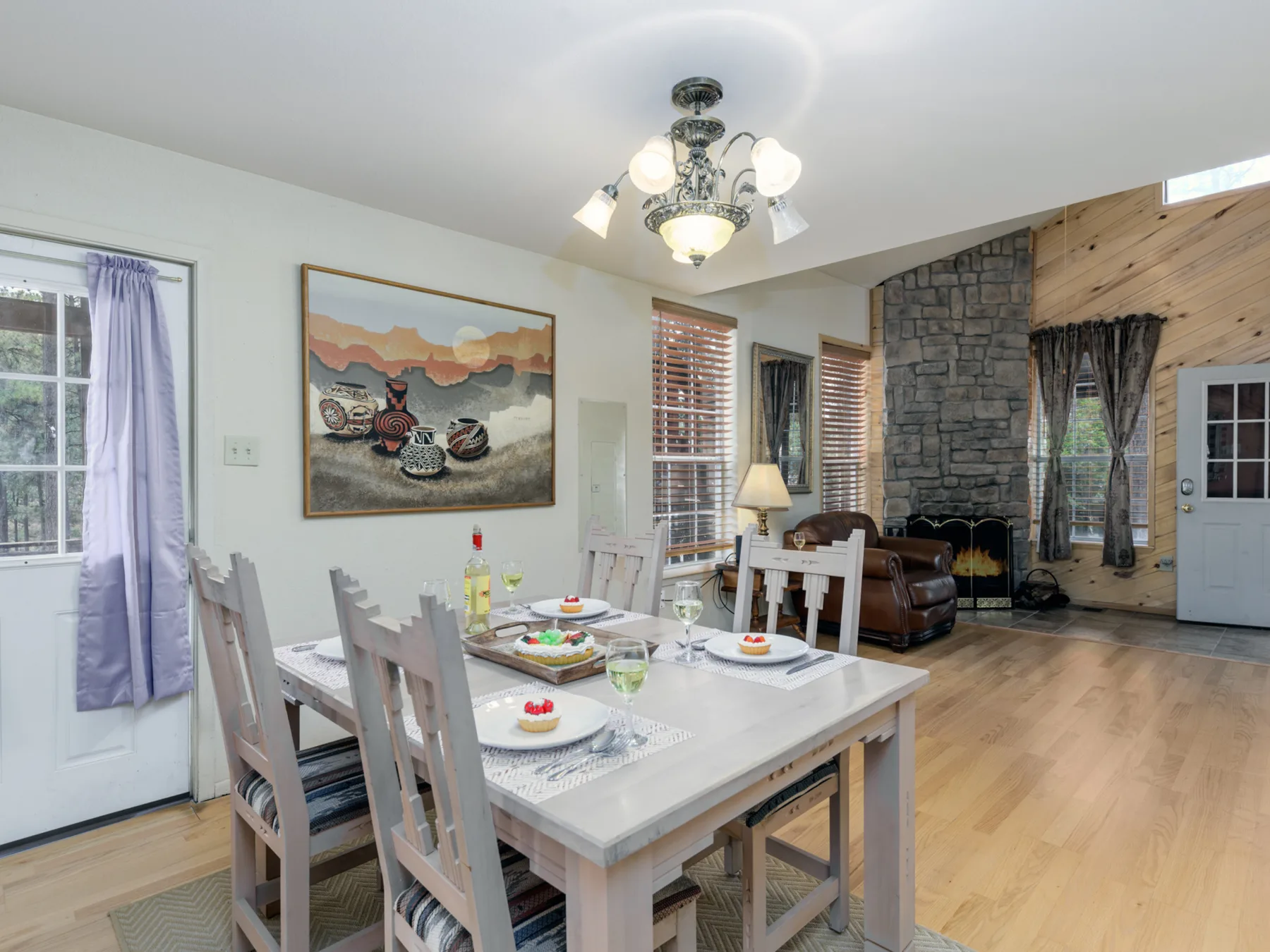 Comedor con la mesa puesta junto a una sala de estar y una chimenea de piedra.