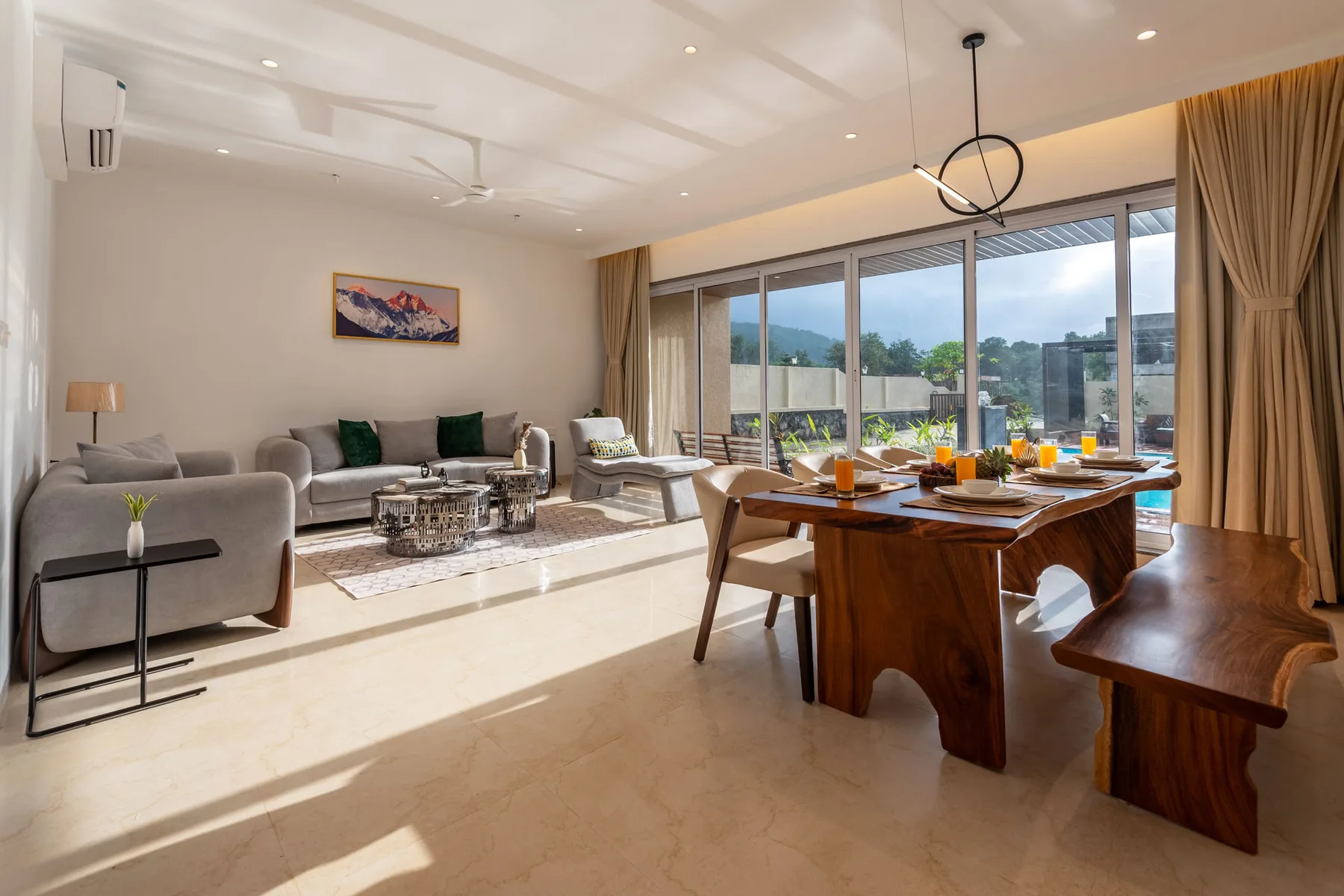 Una luminosa sala de estar y comedor tiene asientos y una mesa de madera junto a grandes ventanas.