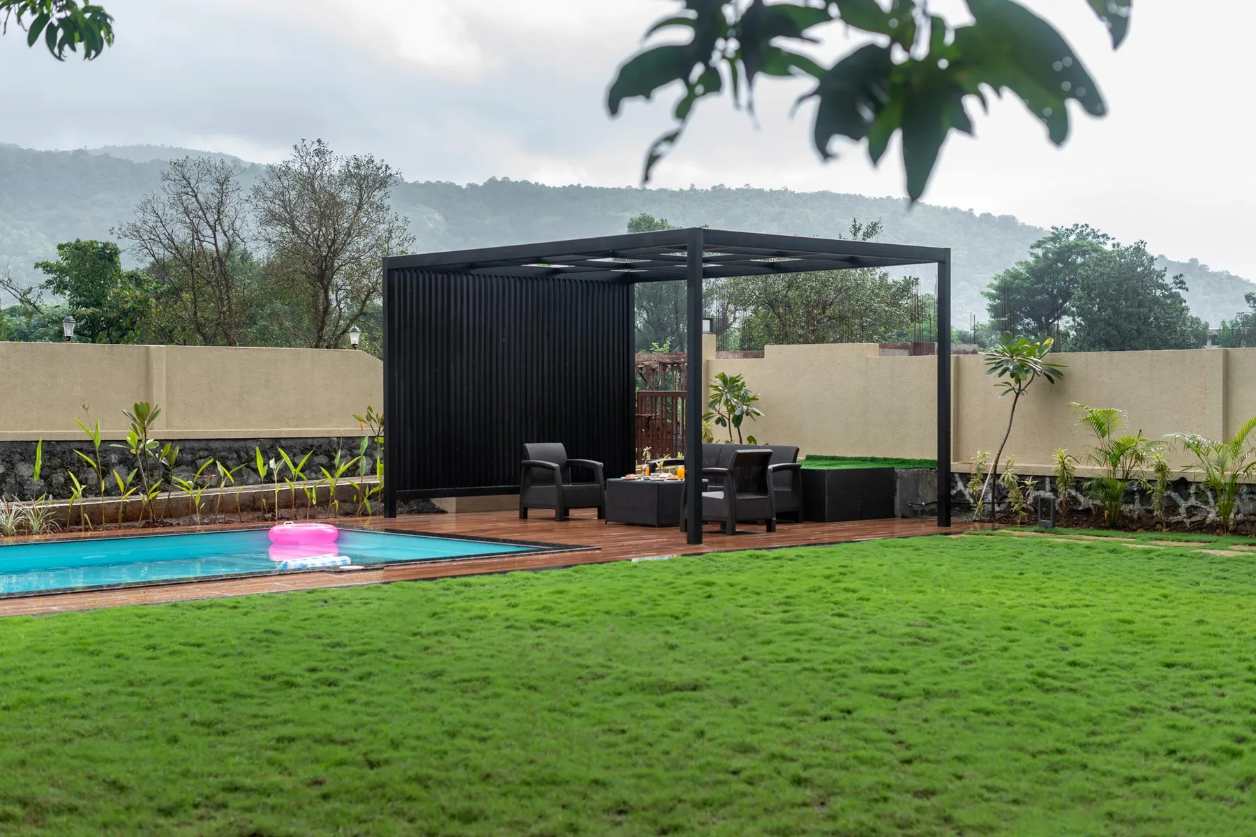 Una piscina ajardinada junto a una zona de estar a la sombra y un césped verde.