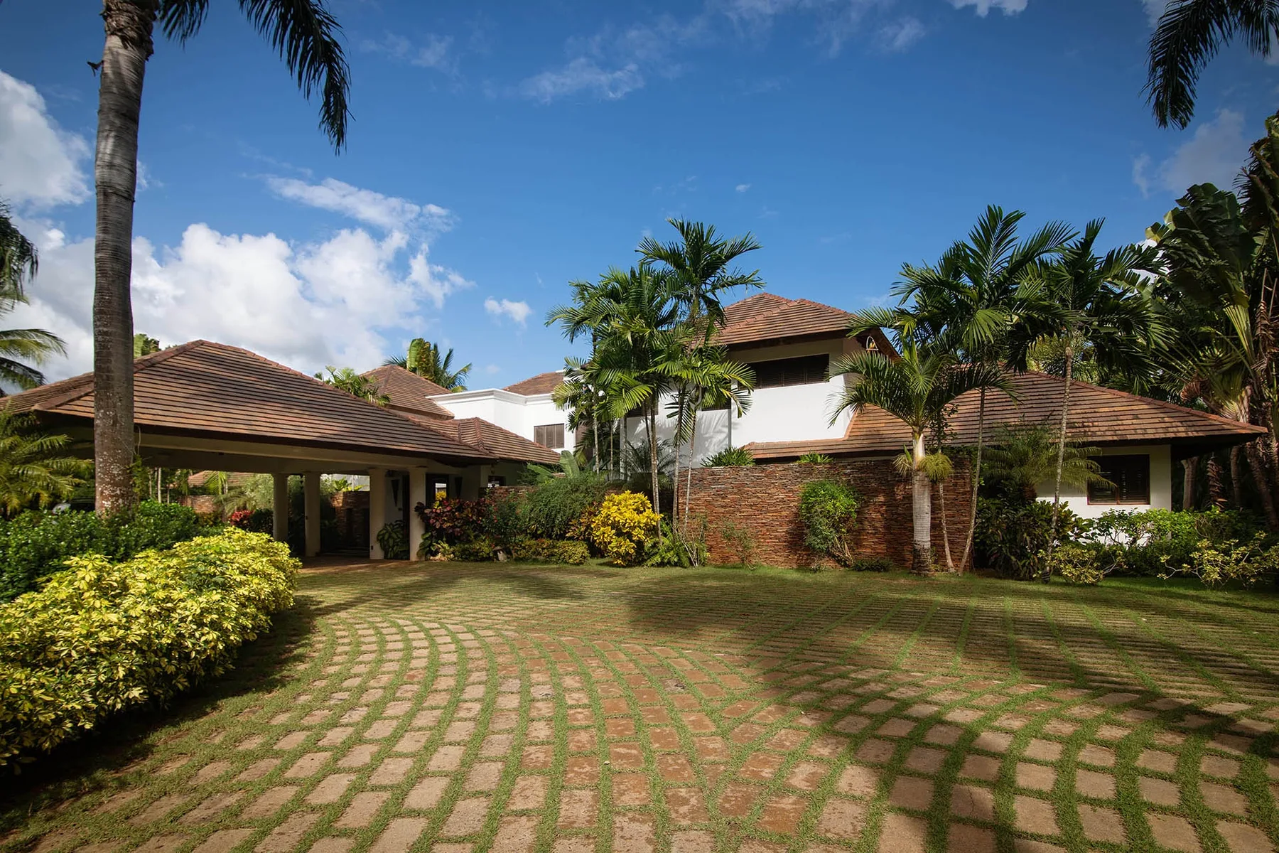 A large house surrounded by tropical landscaping and a patterned grassy driveway.