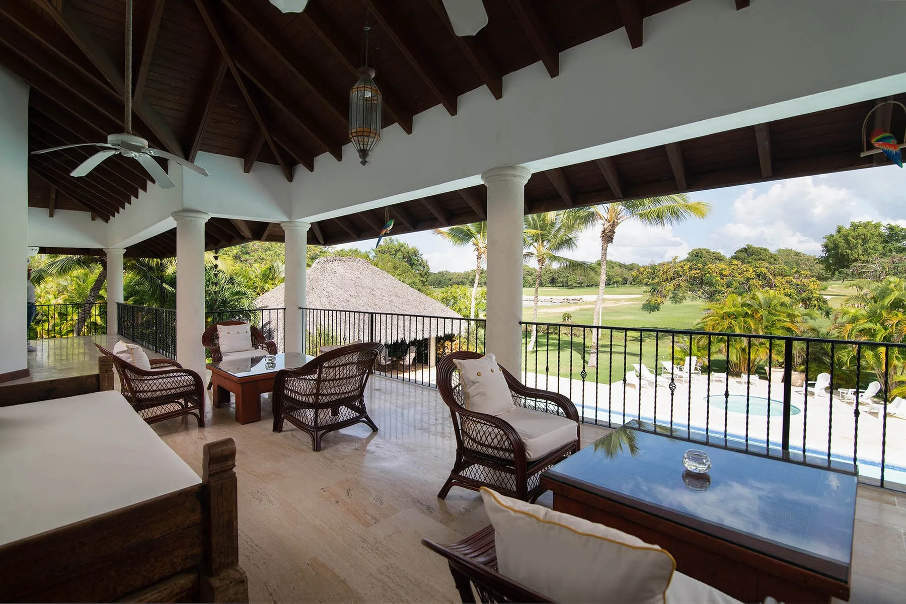 A covered terrace with wicker seating overlooks a garden and pool.
