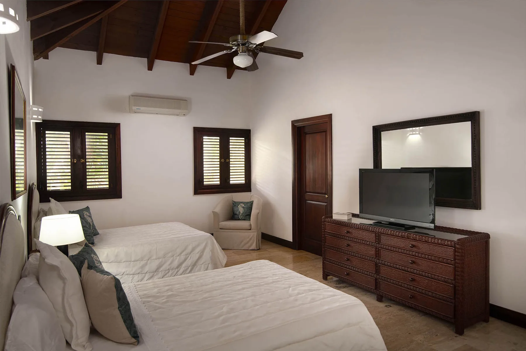 A bedroom with two beds, a television, and a ceiling fan.