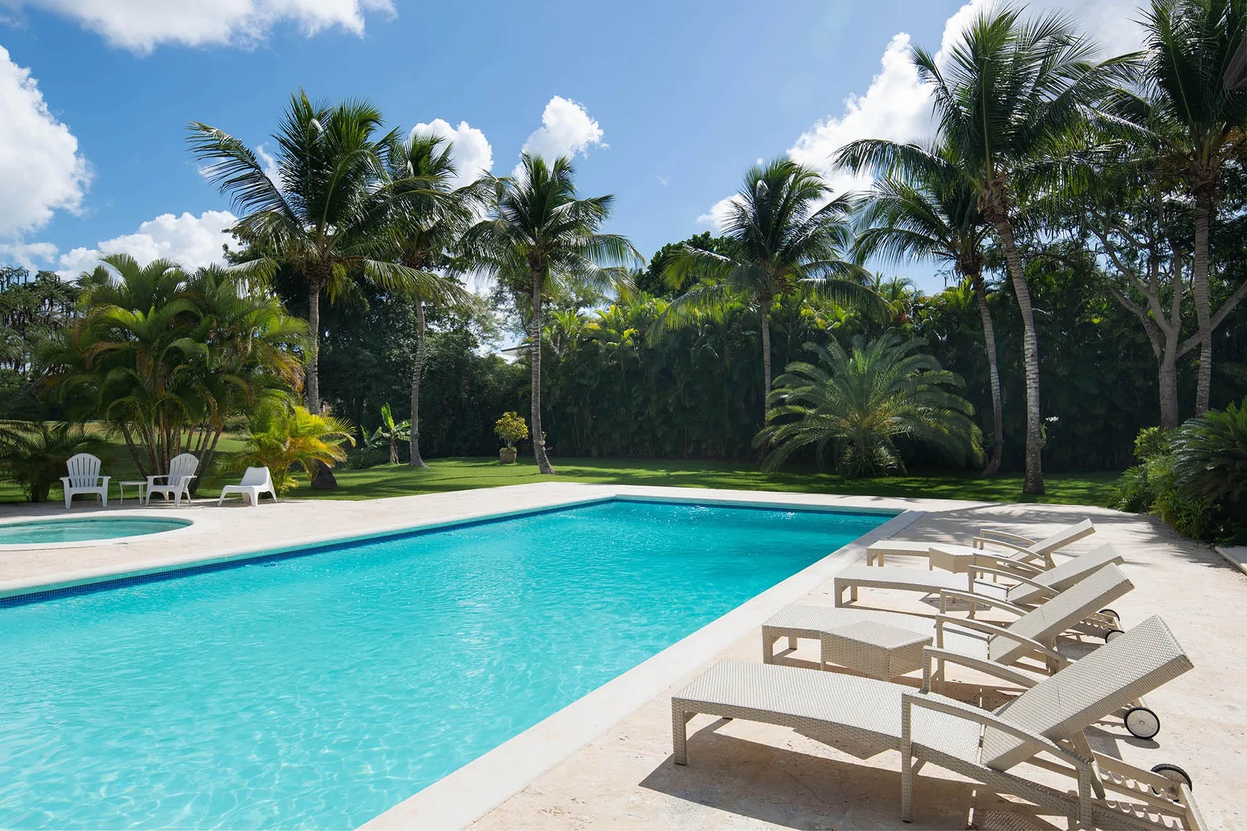 A swimming pool is bordered by lounge seating and palm trees.