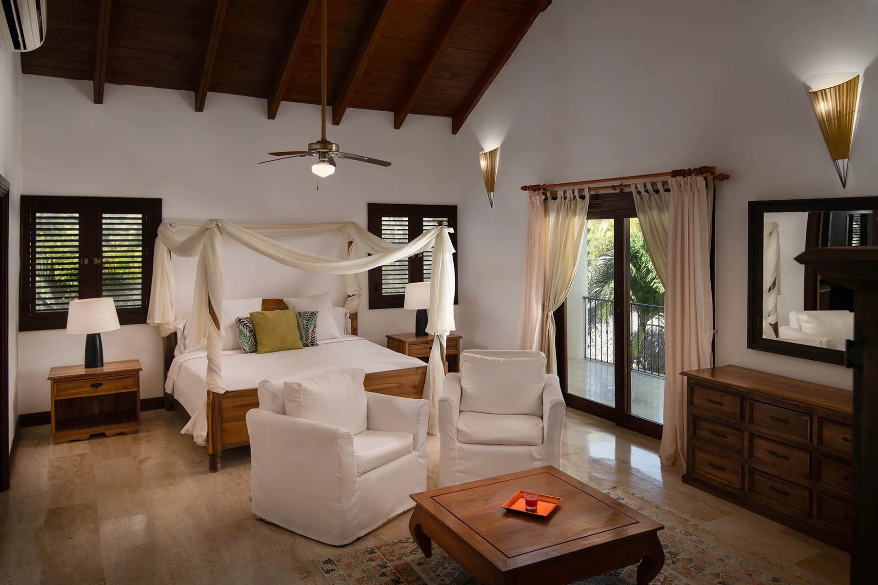 A bedroom with a canopied bed, seating, and glass doors opening to a balcony.