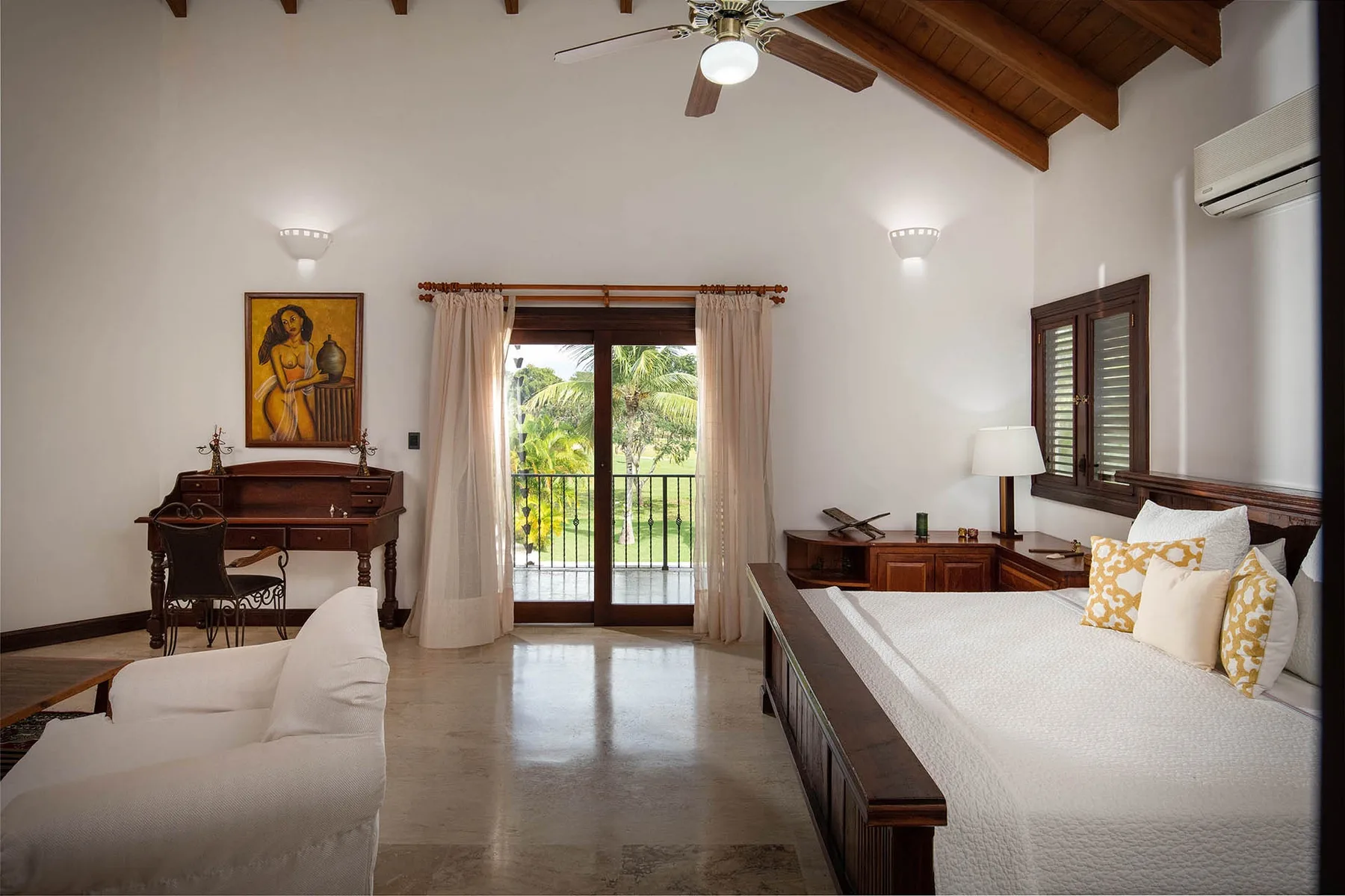 A bright bedroom with a bed, a sitting area, and glass doors opening onto a balcony.