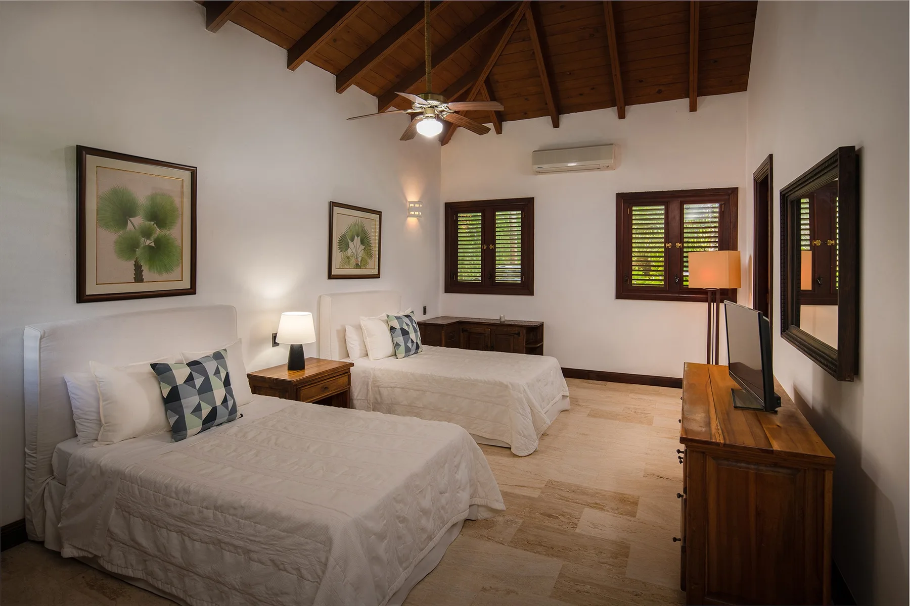 A bedroom with two beds, wooden shutters, and a sloped timber ceiling.