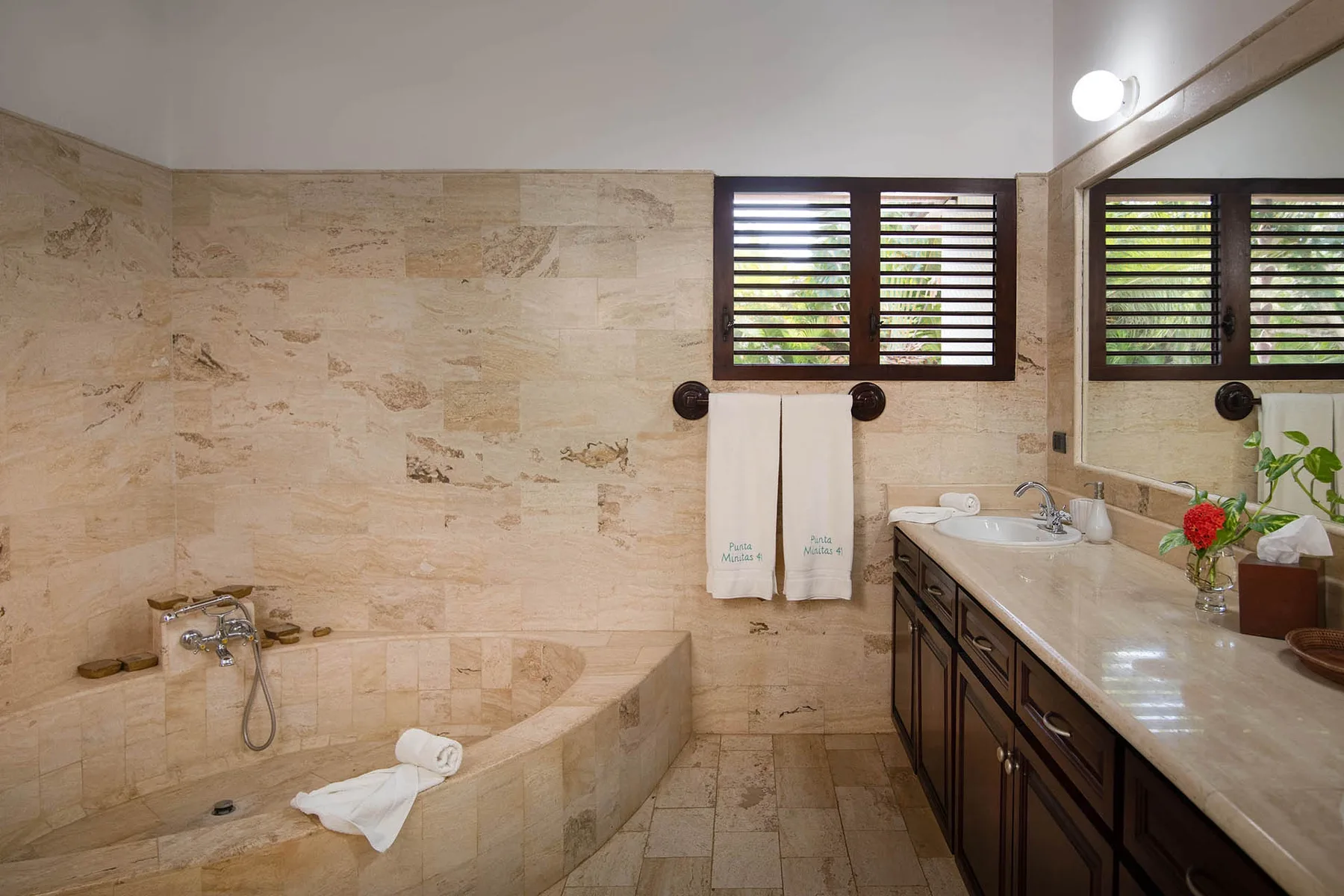 A tiled bathroom with a bathtub, towels, and a long vanity beneath the windows.