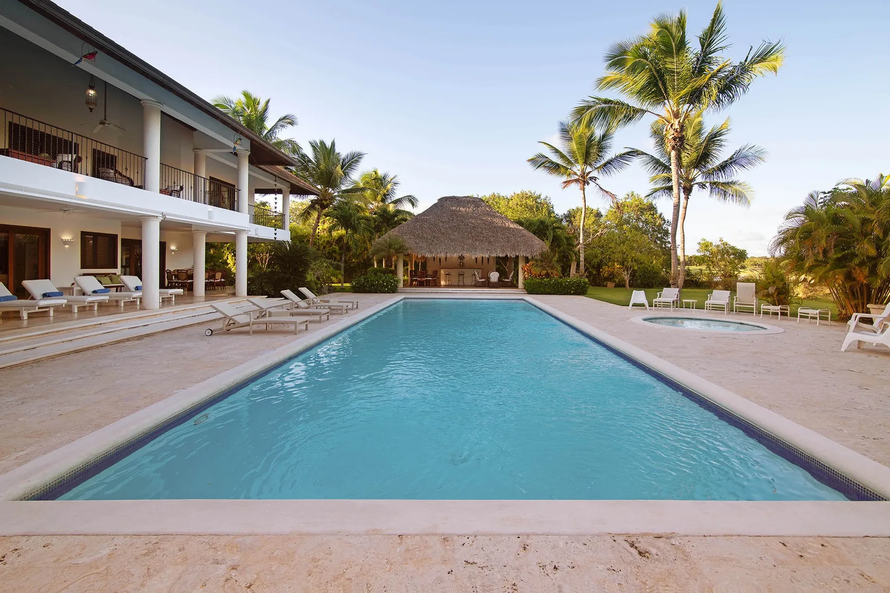 A swimming pool beside a multi-story building, with palm trees and lounge seating.