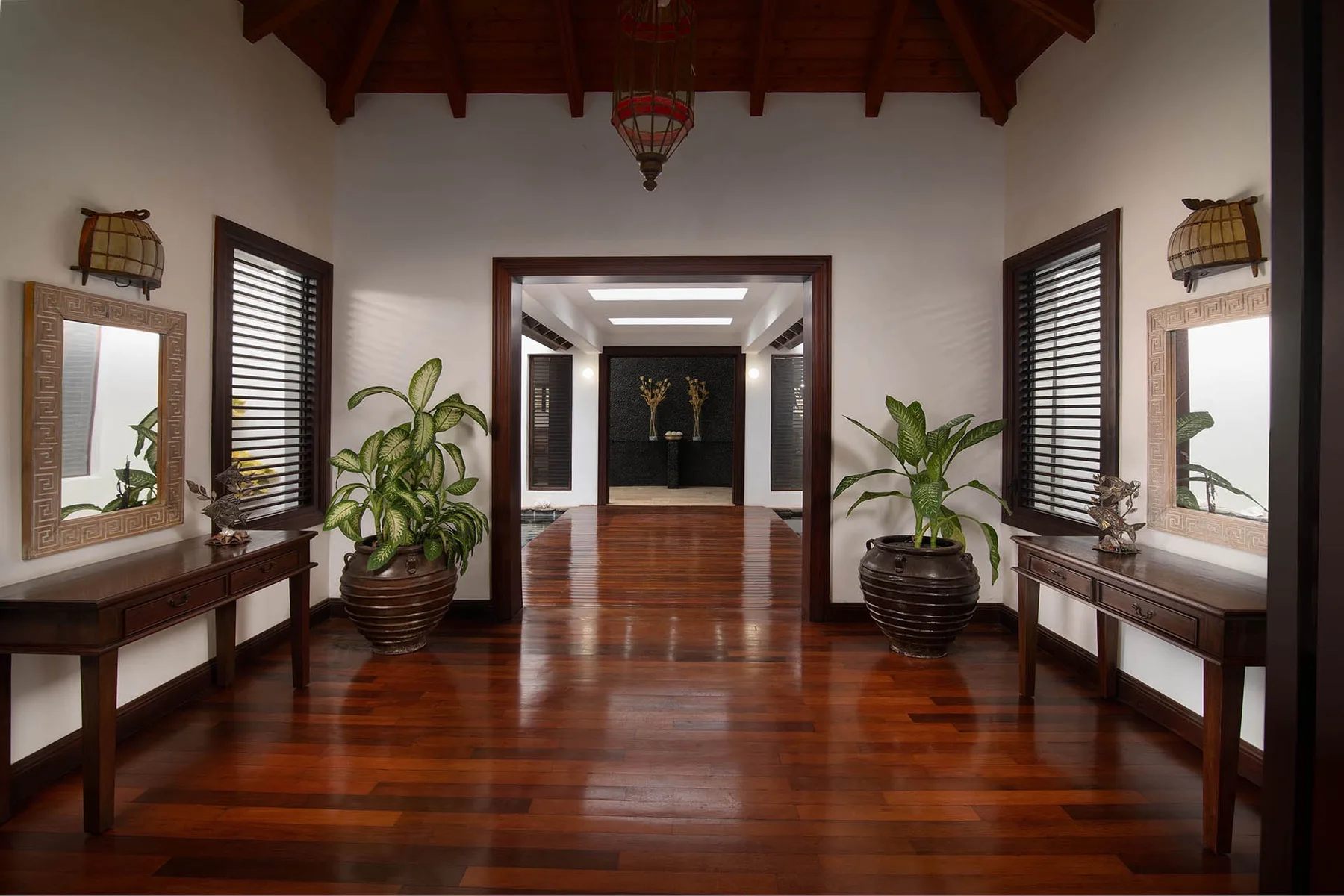 A polished wood-floored hallway opens into another room, with plants beside the doorway.