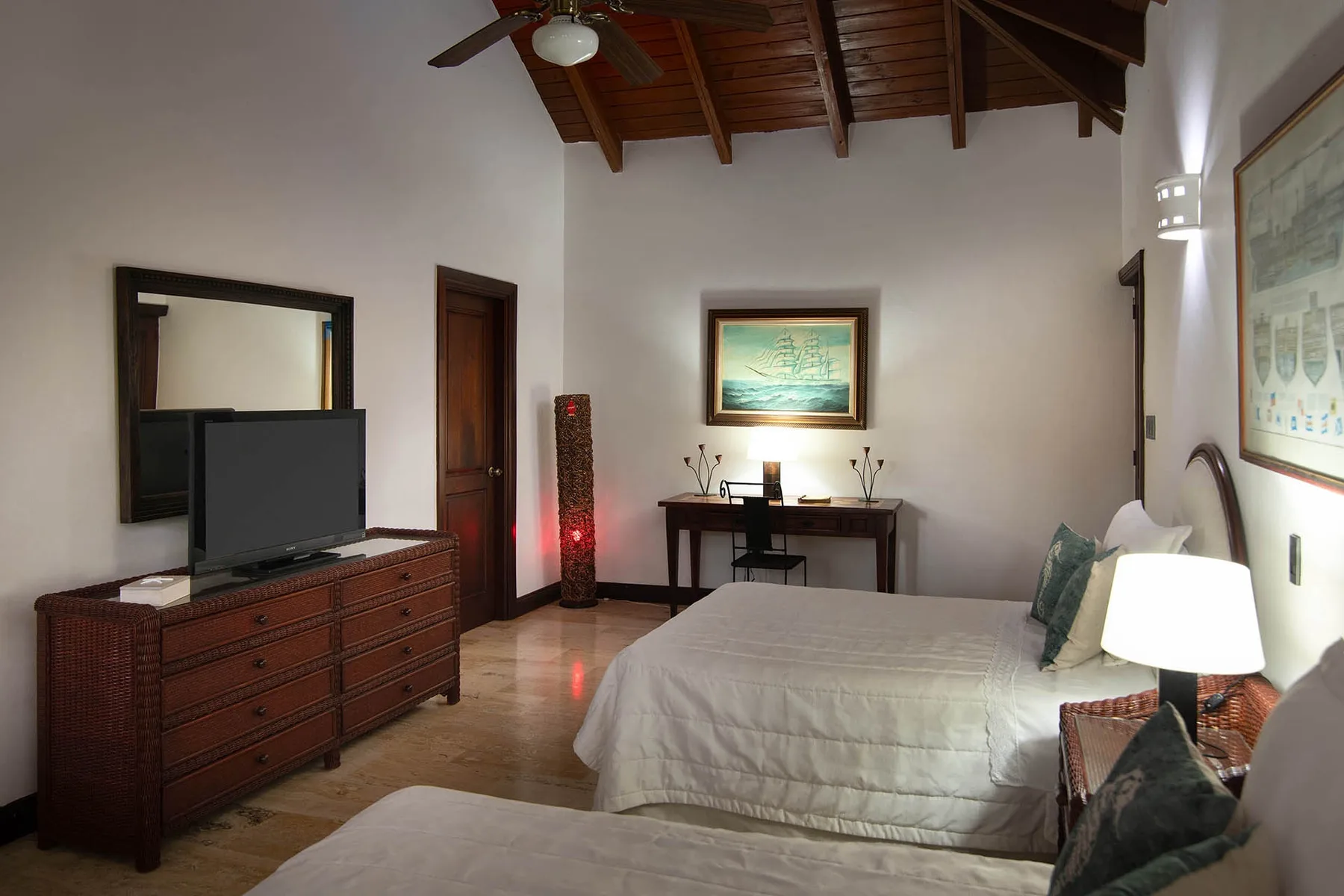 A bedroom with beds, a dresser, and a desk beneath a wood-beamed ceiling.