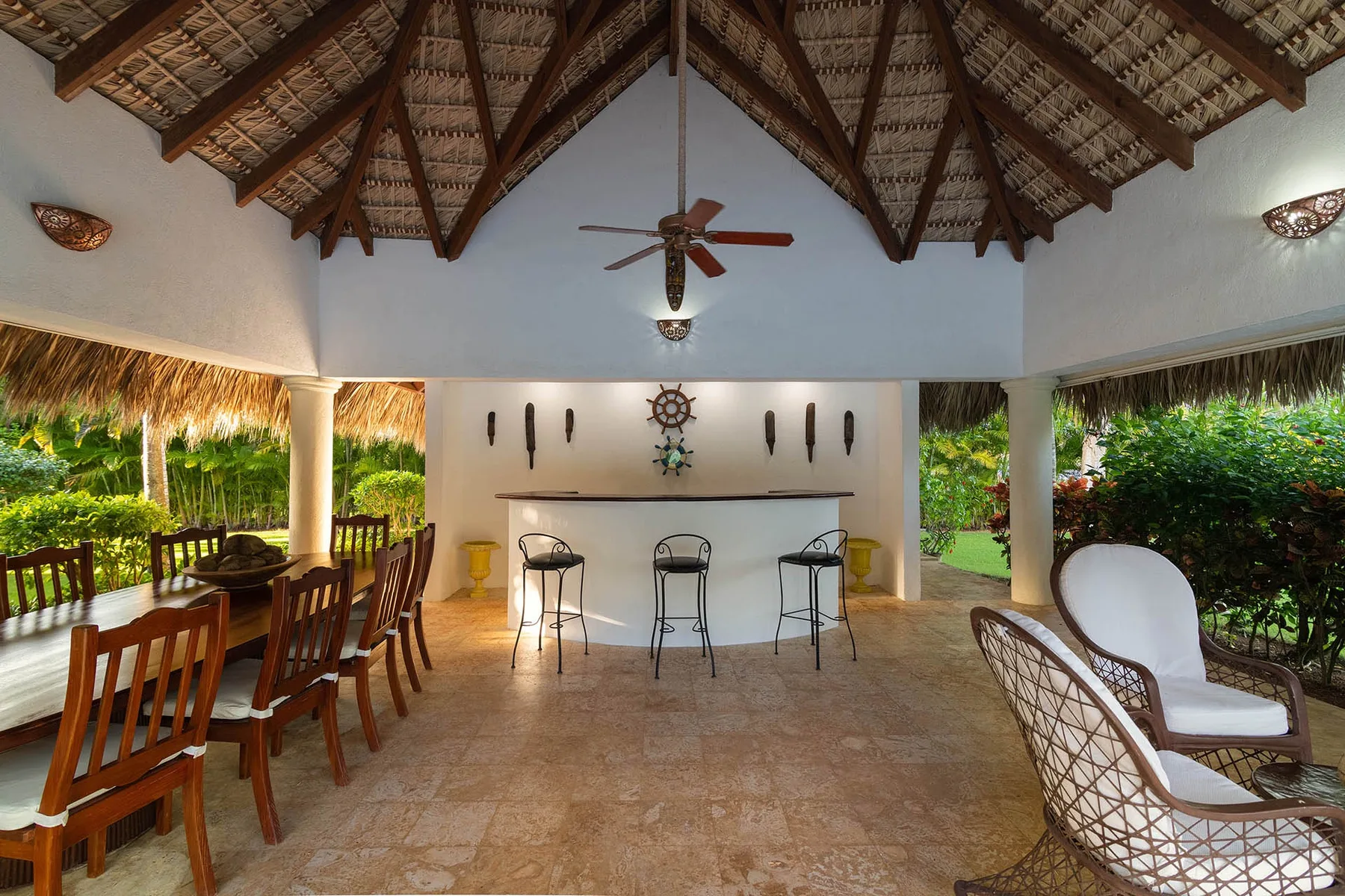 An open-air dining and seating area beneath a high thatched roof.
