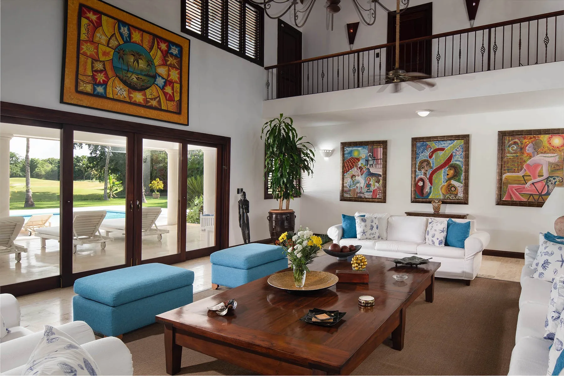 A bright living room with a white seating area, blue ottomans, and a large wooden coffee table.
