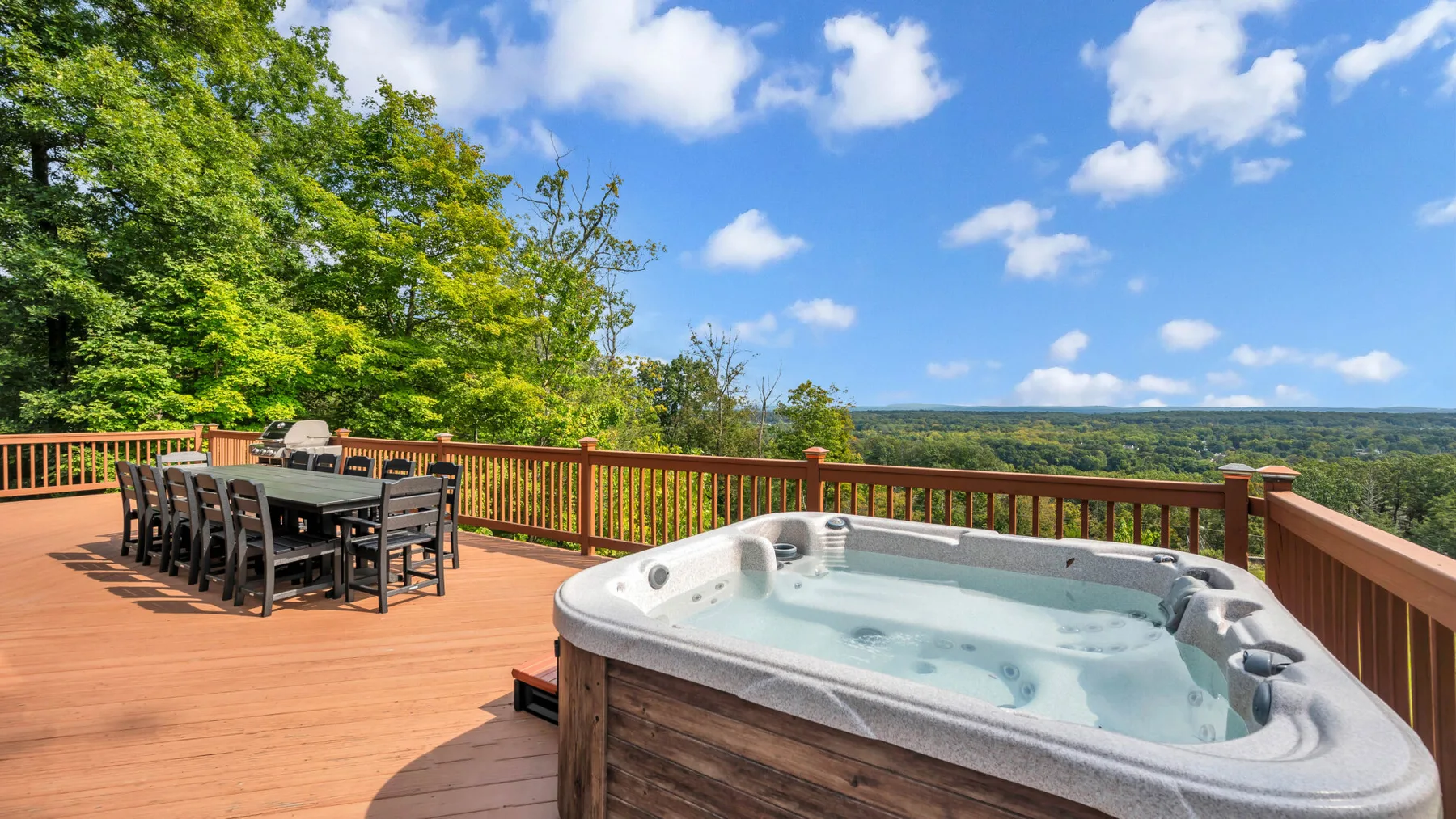 An outdoor deck features a hot tub and dining table overlooking a wooded landscape.
