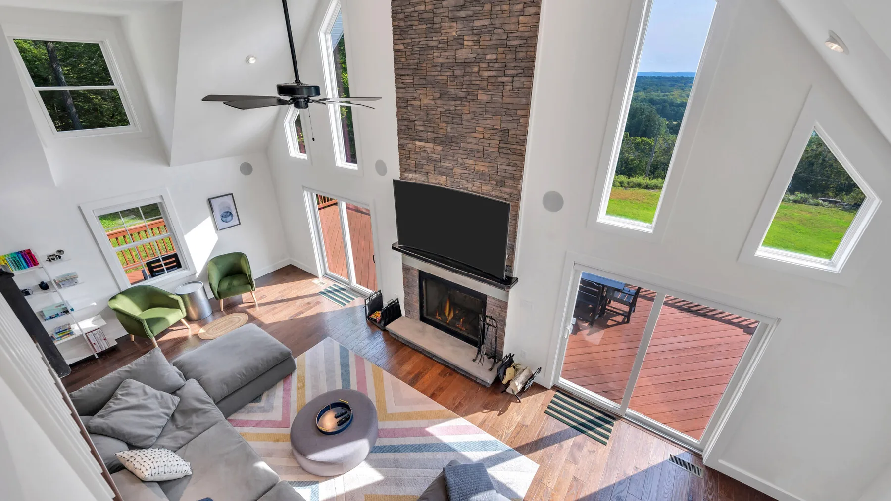 A bright living room with a seating area, fireplace, and windows overlooking a deck.