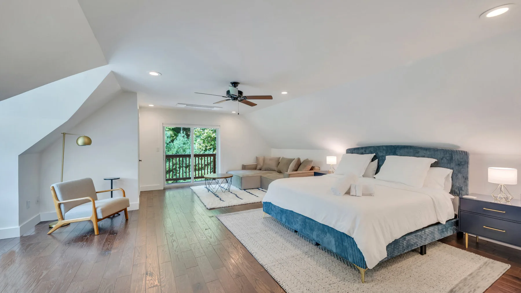 A bright bedroom with a large bed, seating area, and balcony doors.