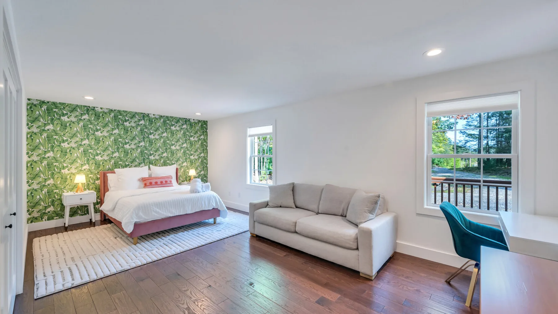 A bedroom and sitting area with a bed, sofa, and leafy accent wall.