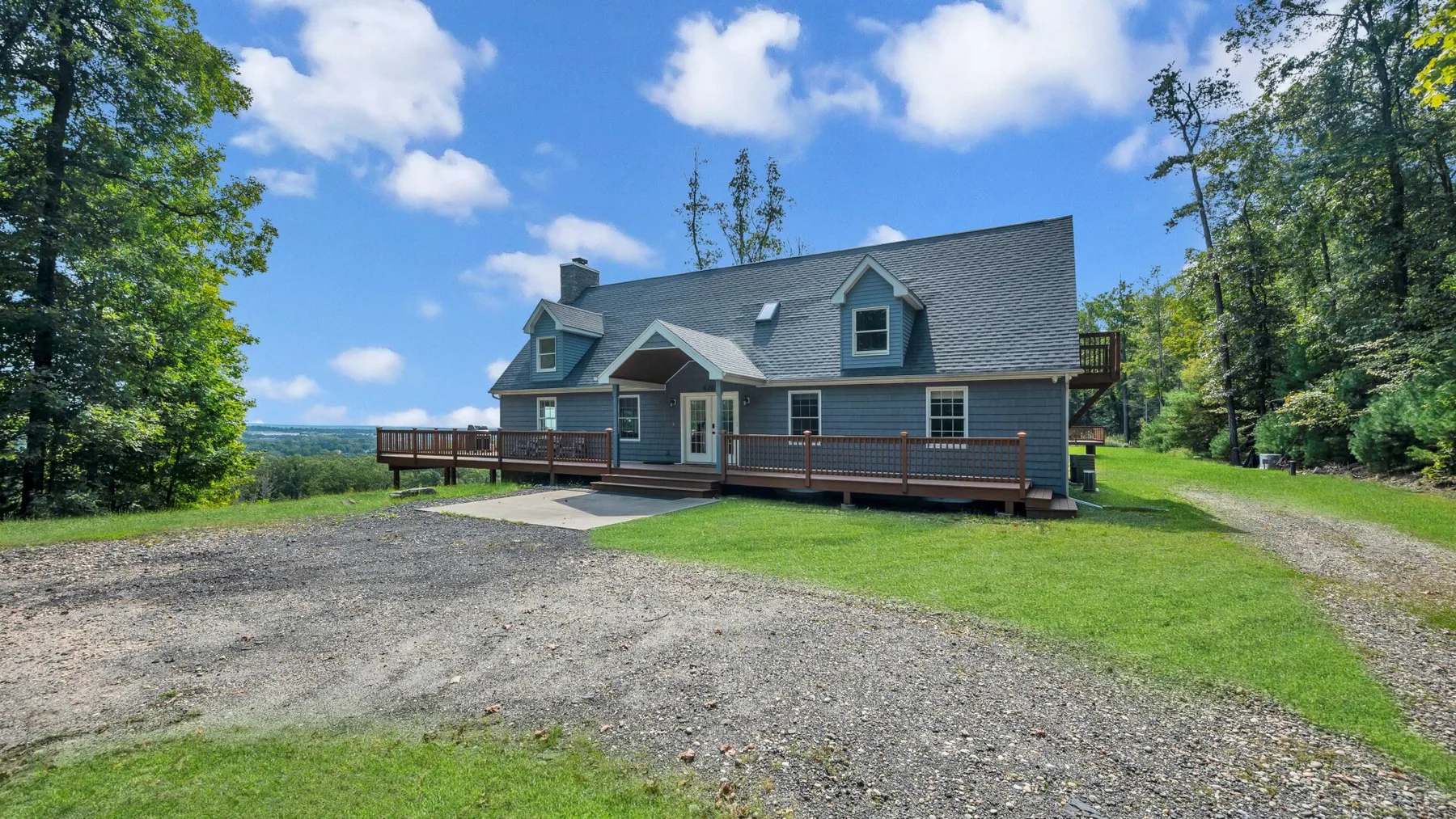 A gray house with a broad gravel driveway and green lawn.