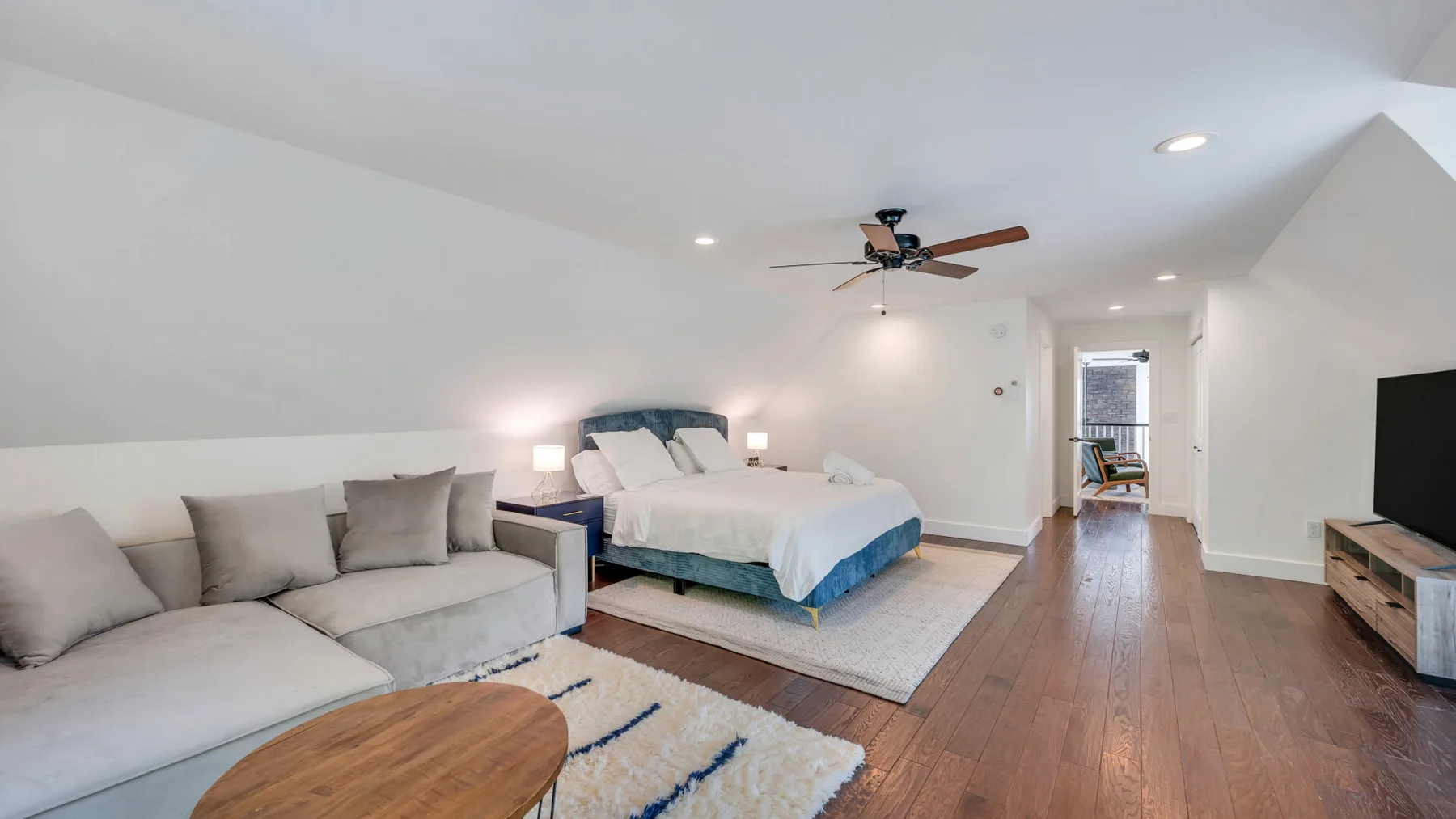 A bright bedroom with a bed, seating area, and wooden floor.