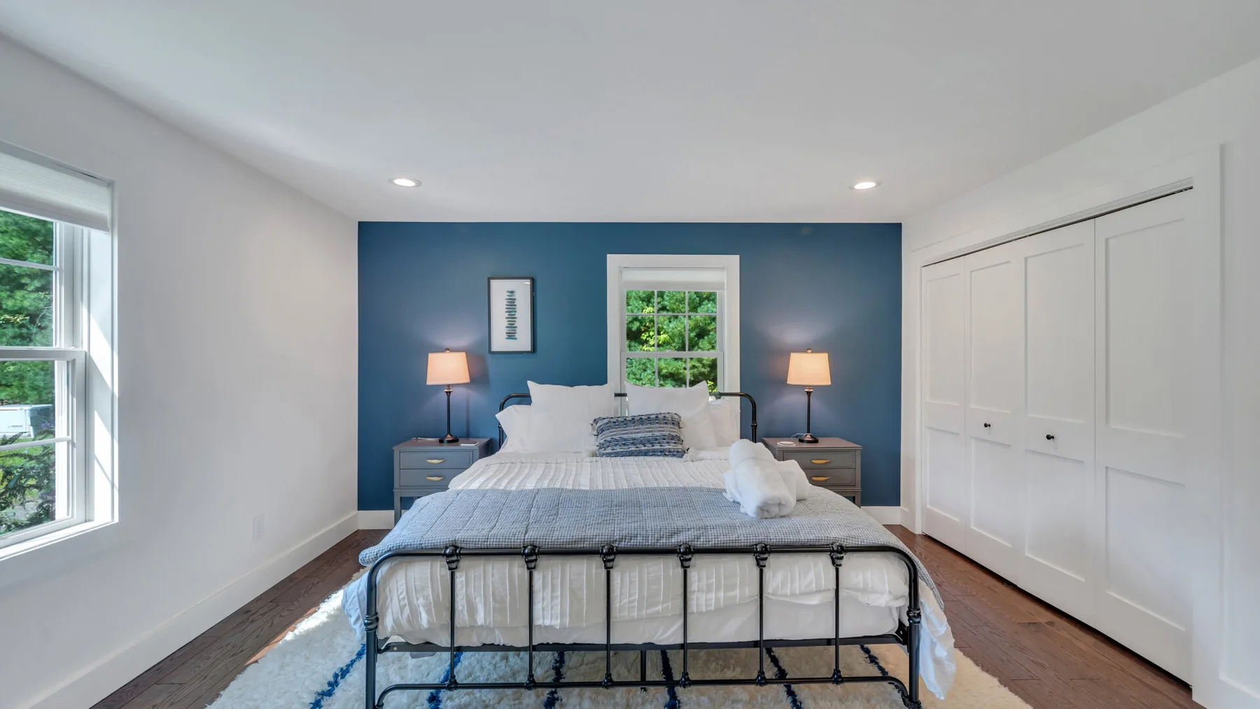 A bedroom with a bed against a blue accent wall and white closets.