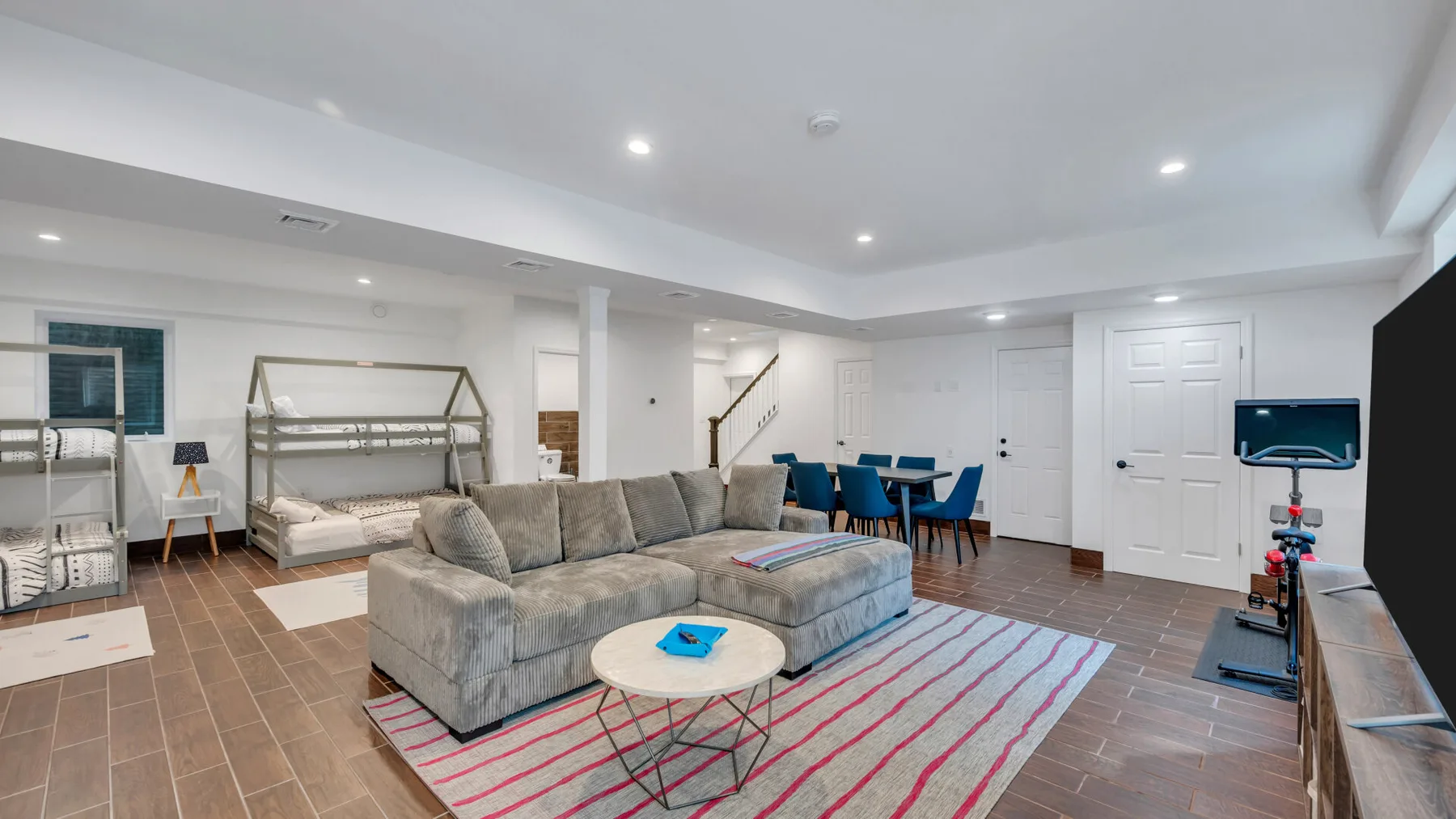 A basement living area with seating, a dining table, and a television.