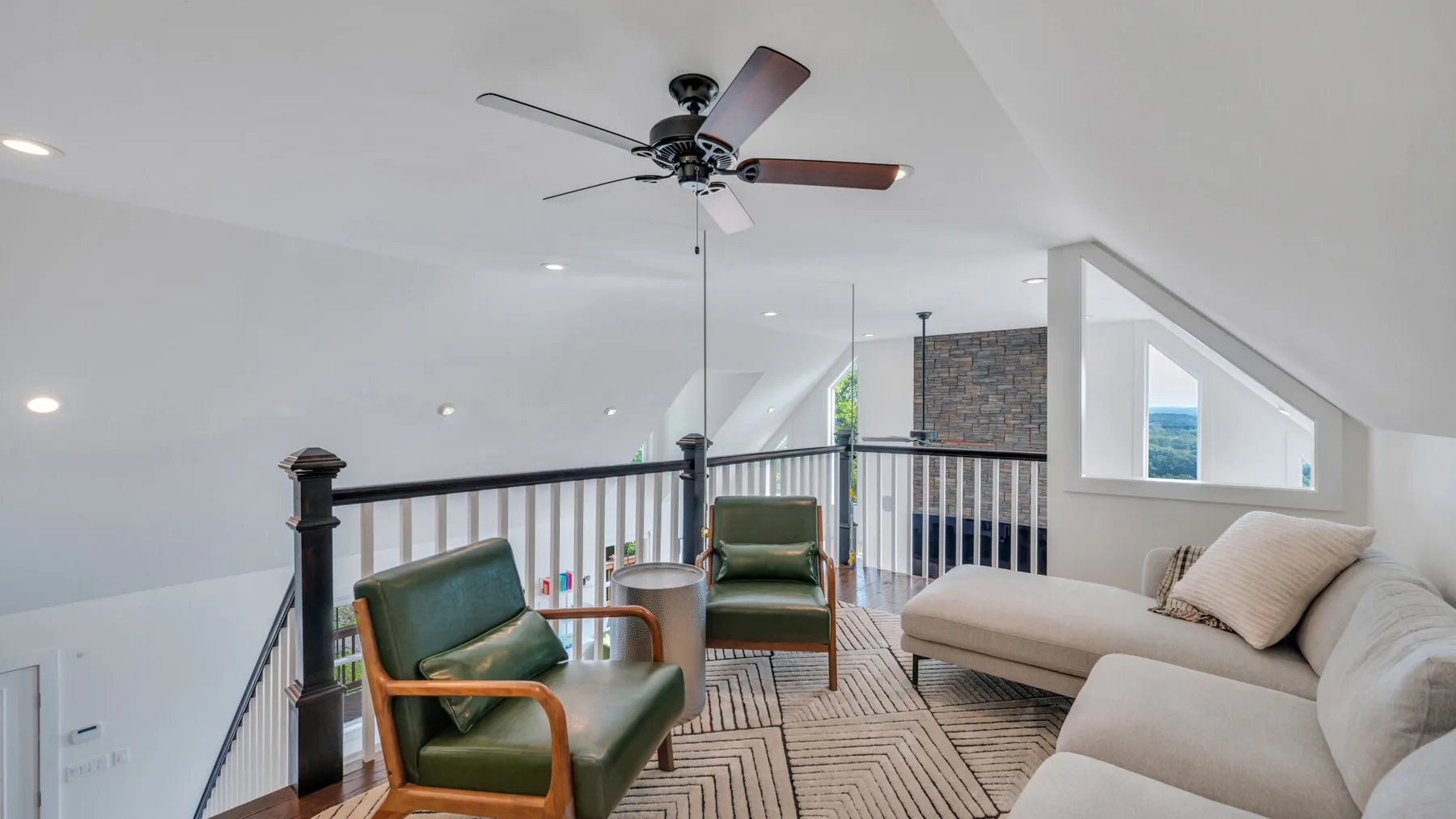A loft sitting area with green seating and a light-colored sectional sofa.