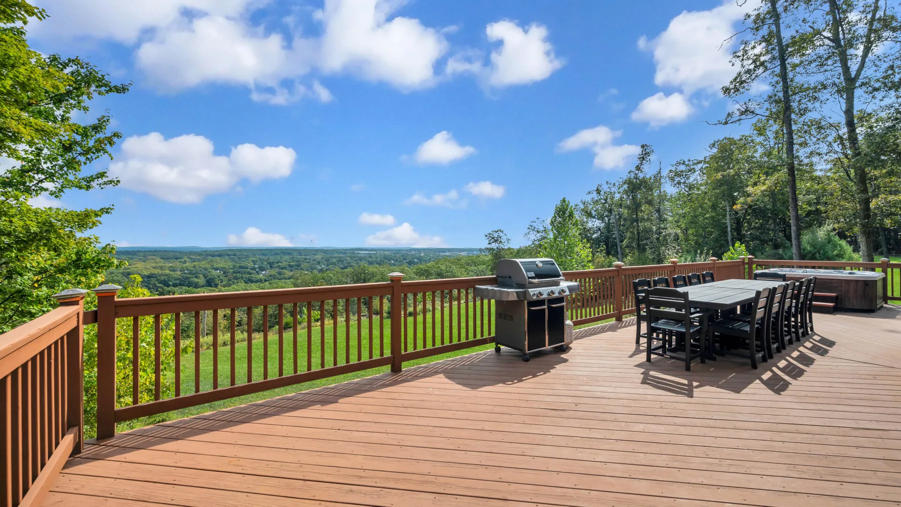An outdoor deck with a dining table, grill, and wooded landscape view.