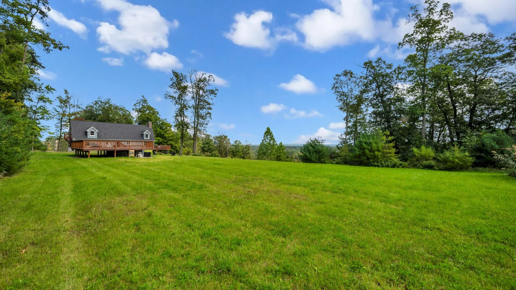 A house stands beyond a broad green lawn, with trees beneath a blue sky.