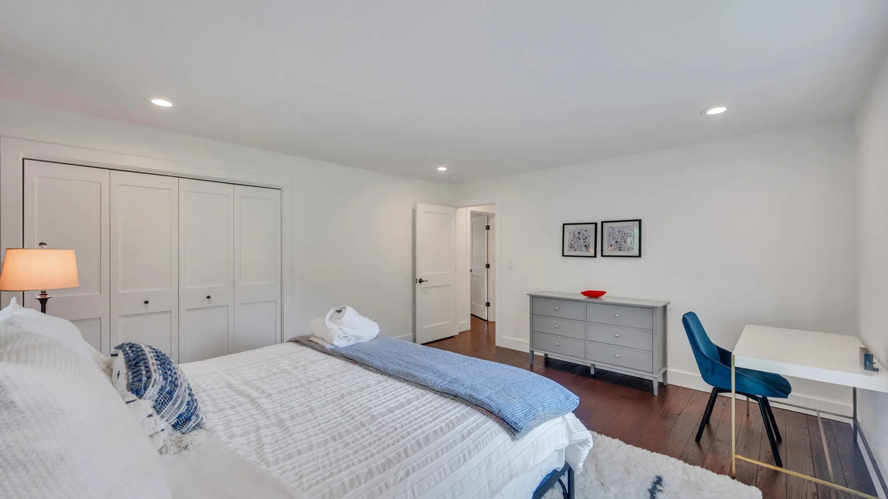 A bright bedroom with a large bed, dresser, and desk.