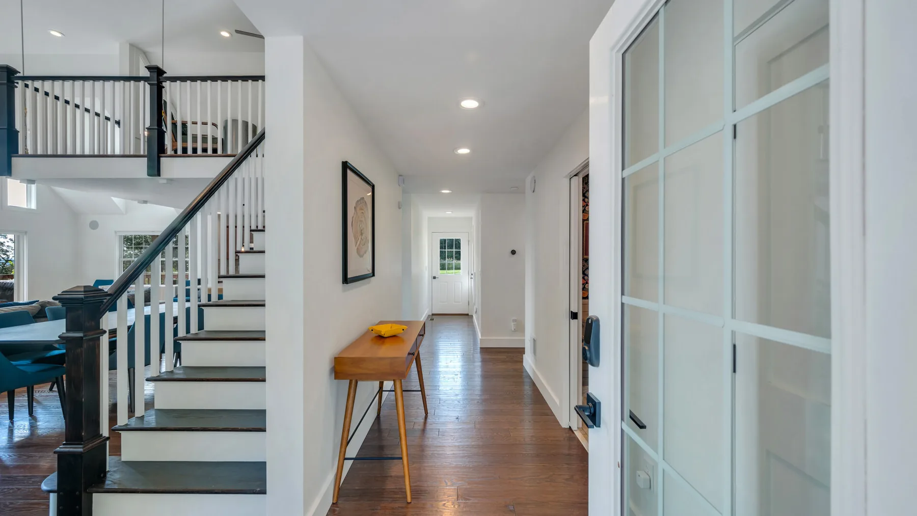 A bright hallway with a wooden console table and a staircase beside the dining area.