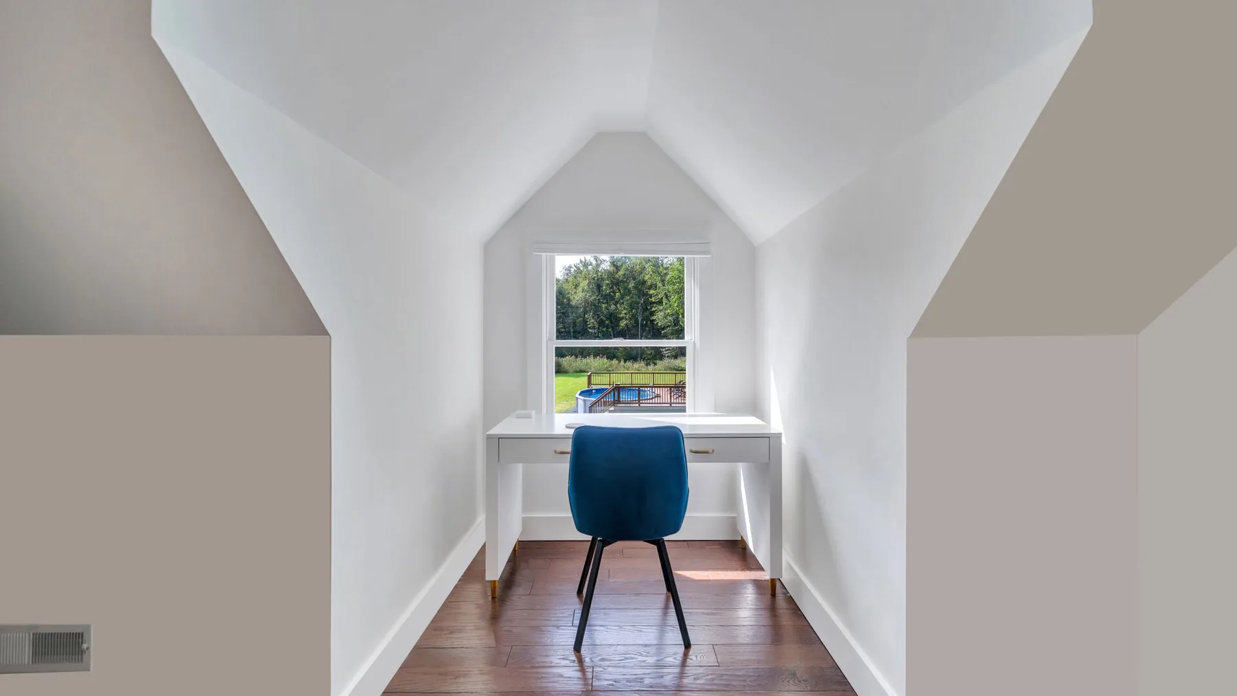 A small desk and chair sit beneath a window in a bright attic room.