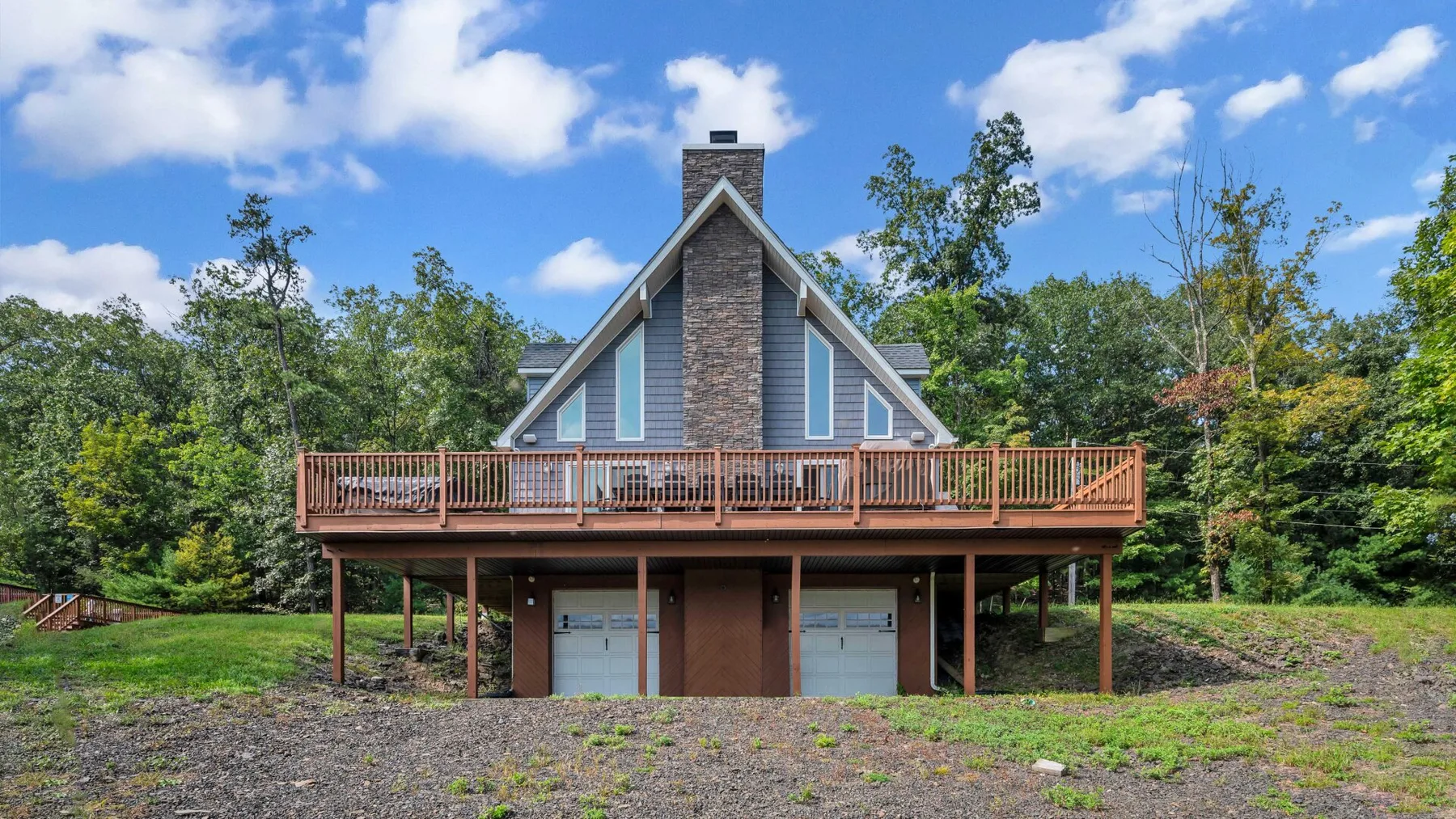A house with a steep gabled roof and a raised wooden deck stands among trees.