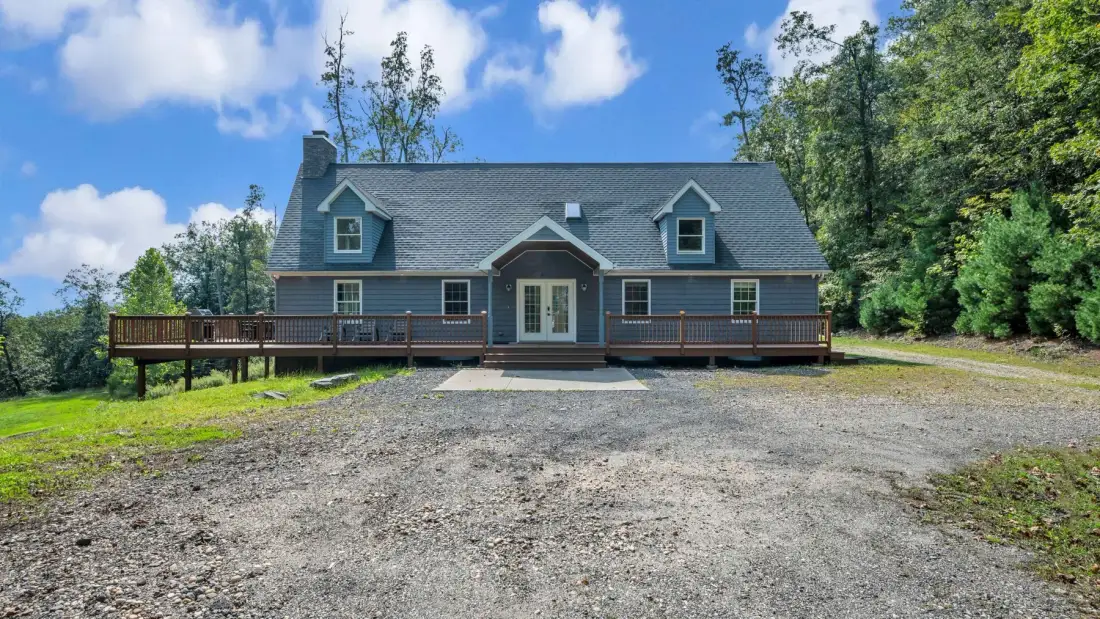 A large house with a gravel driveway and trees surrounding the property.