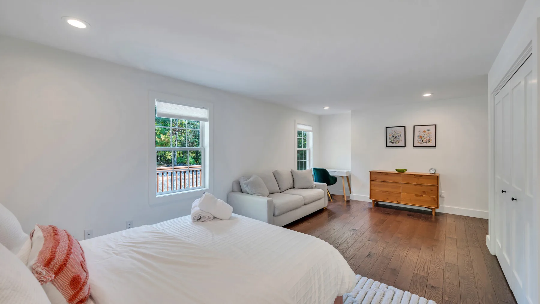 A bright bedroom with a bed, a seating area, and a wooden dresser.