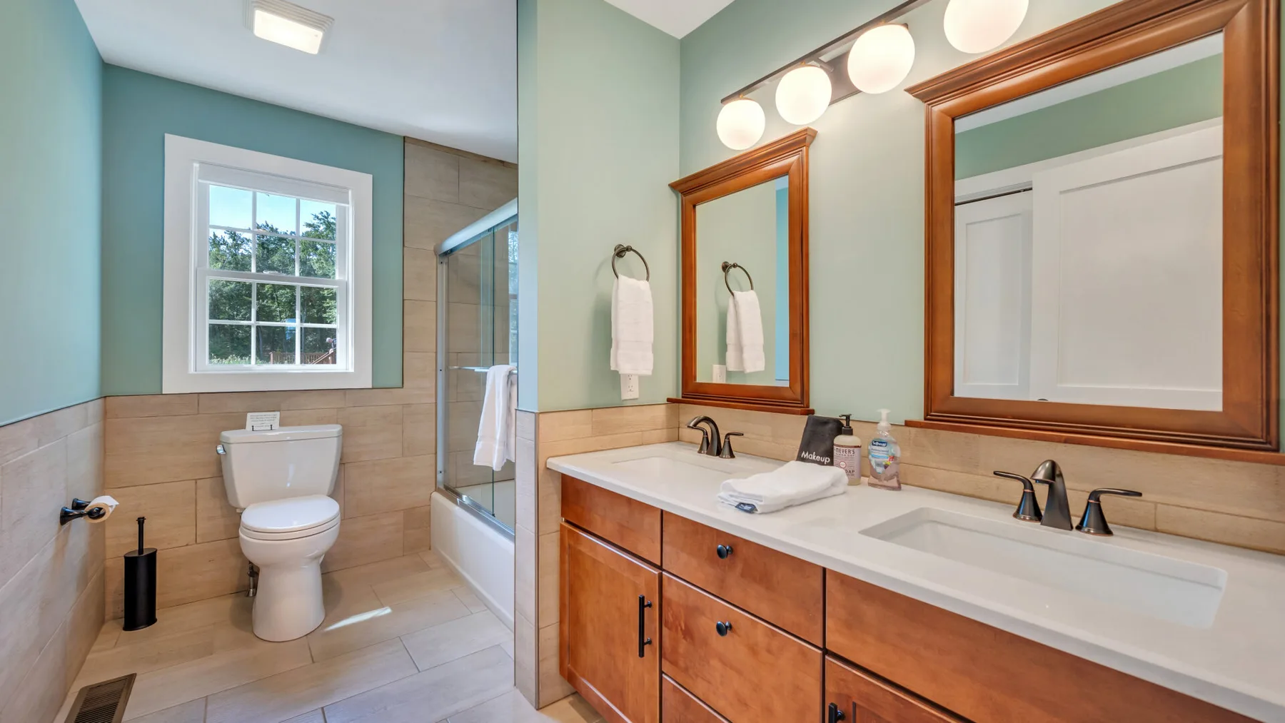 A bathroom with a double vanity, mirrors, and a toilet beside a shower.