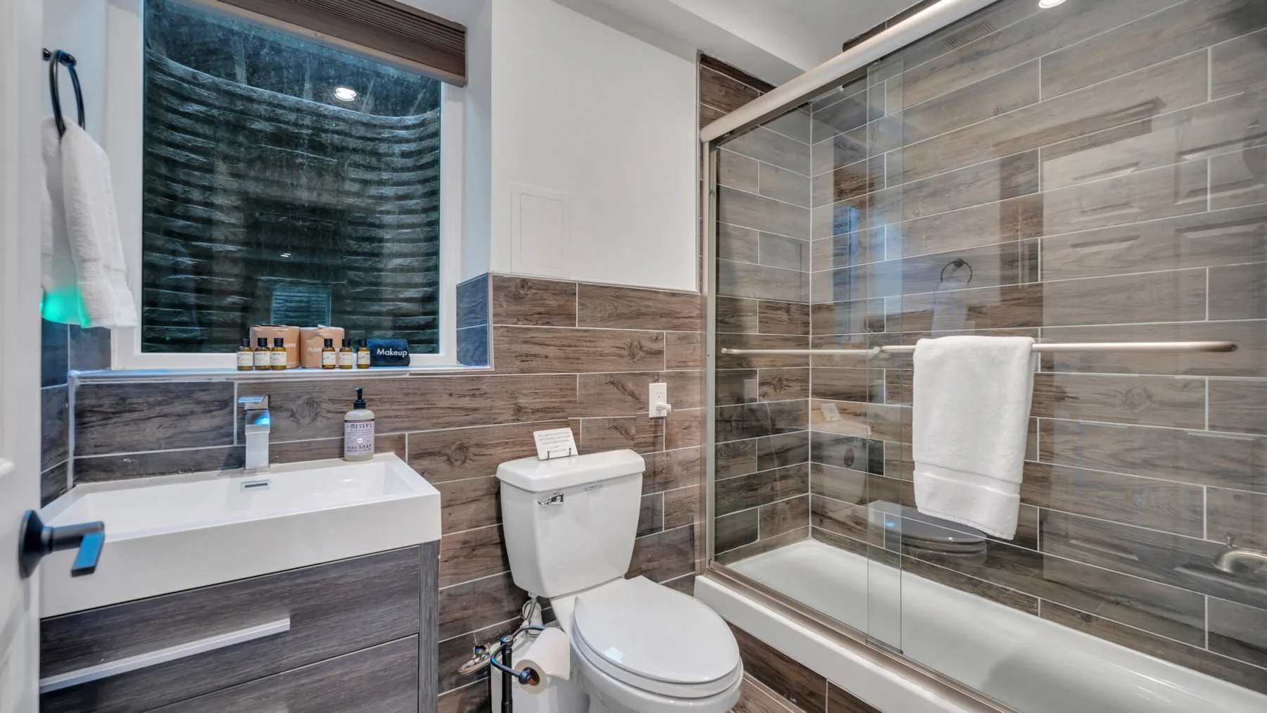 A bathroom with a glass-enclosed shower and a window above the sink.