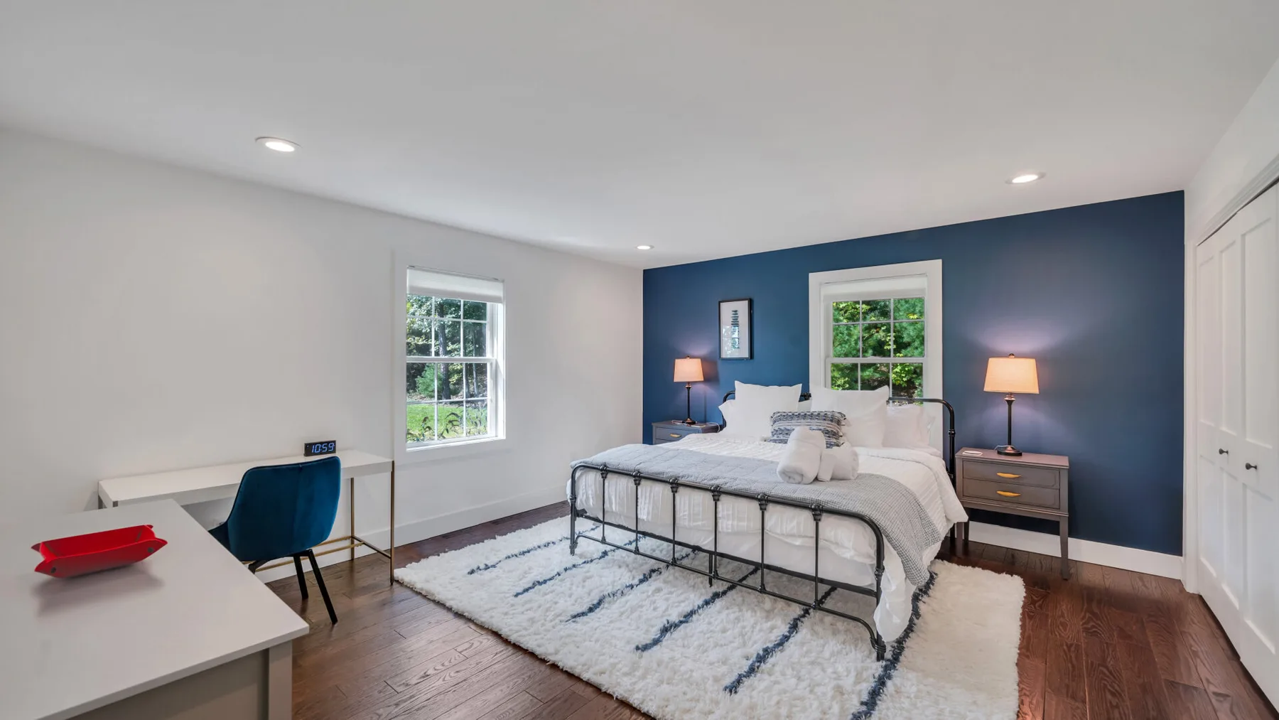 A bedroom with a bed against a dark blue wall and a light rug.